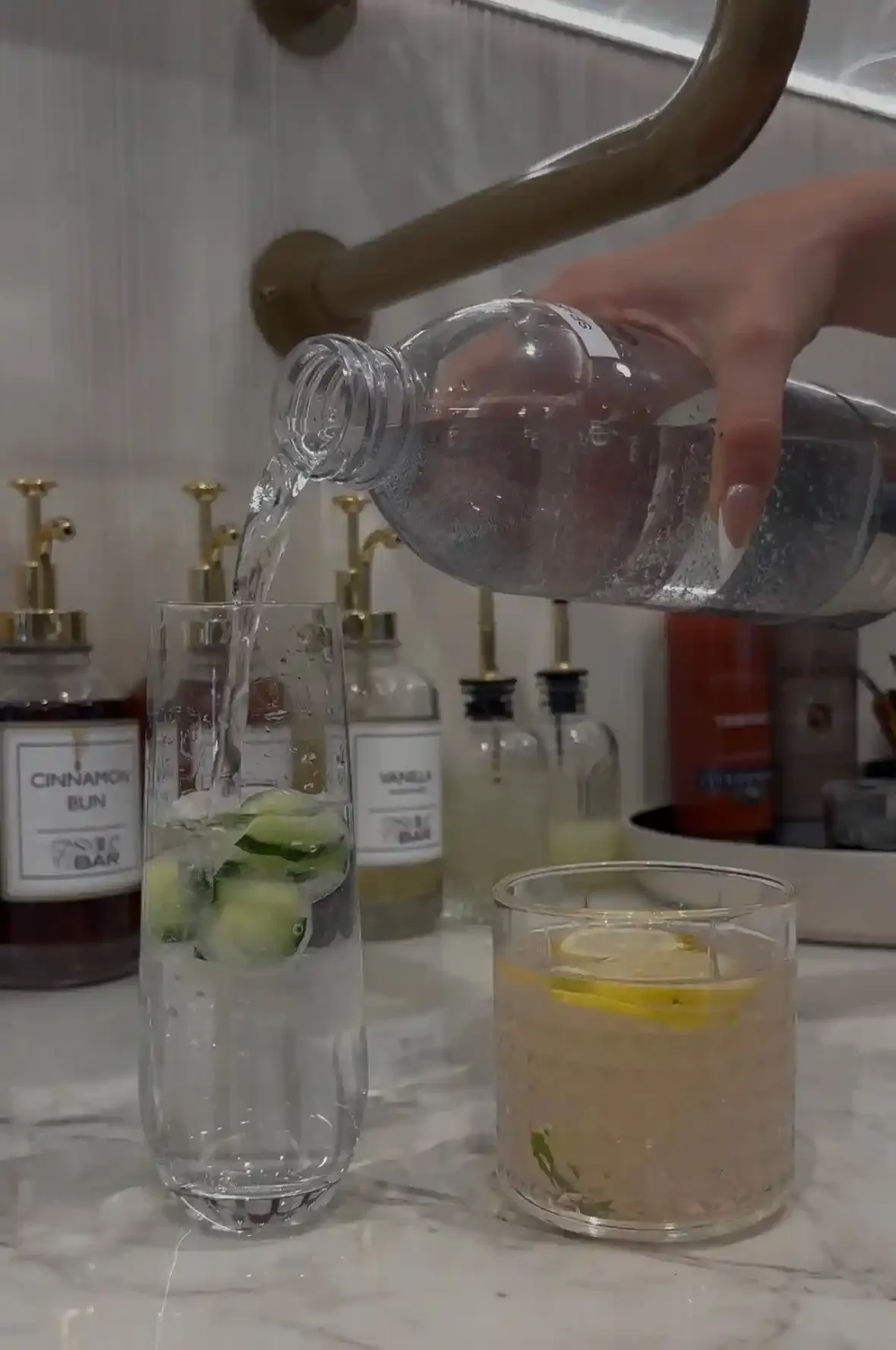 Text: Hand pouring sparkling water into a glass with cucumber slices, showcasing the concierge drink menu at Smile Bar in Calgary.