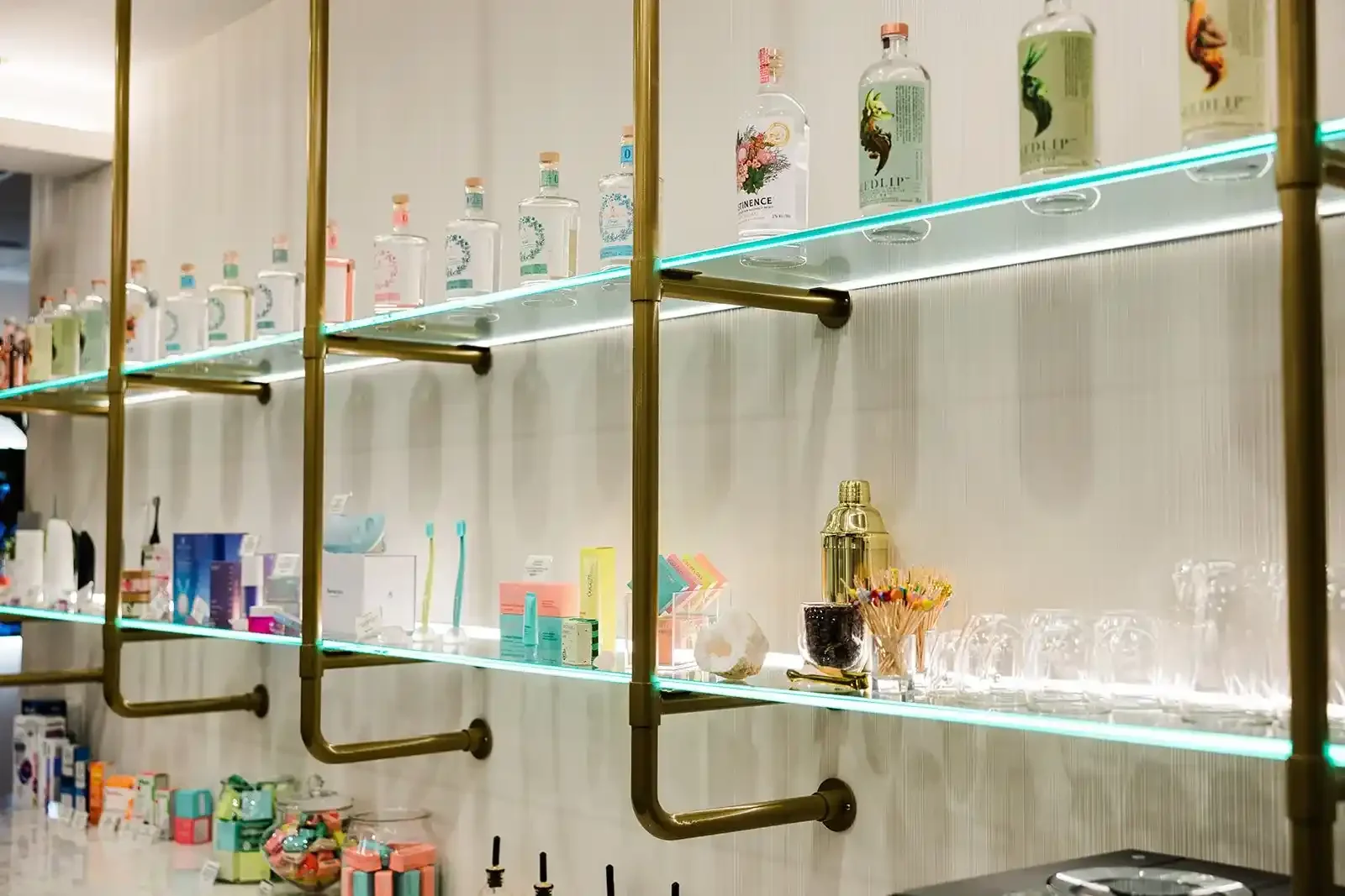 Brass and glass shelving displaying non-alcoholic spirits, a cocktail shaker, and premium dental care products at Smile Bar in Calgary.