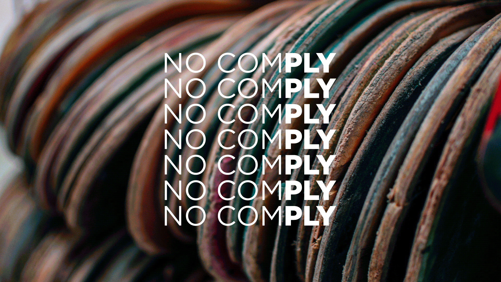 Close-up of broken skateboards stacked upright with a text overlay that reads 'NO COMPLY' repeated multiple times in white font.