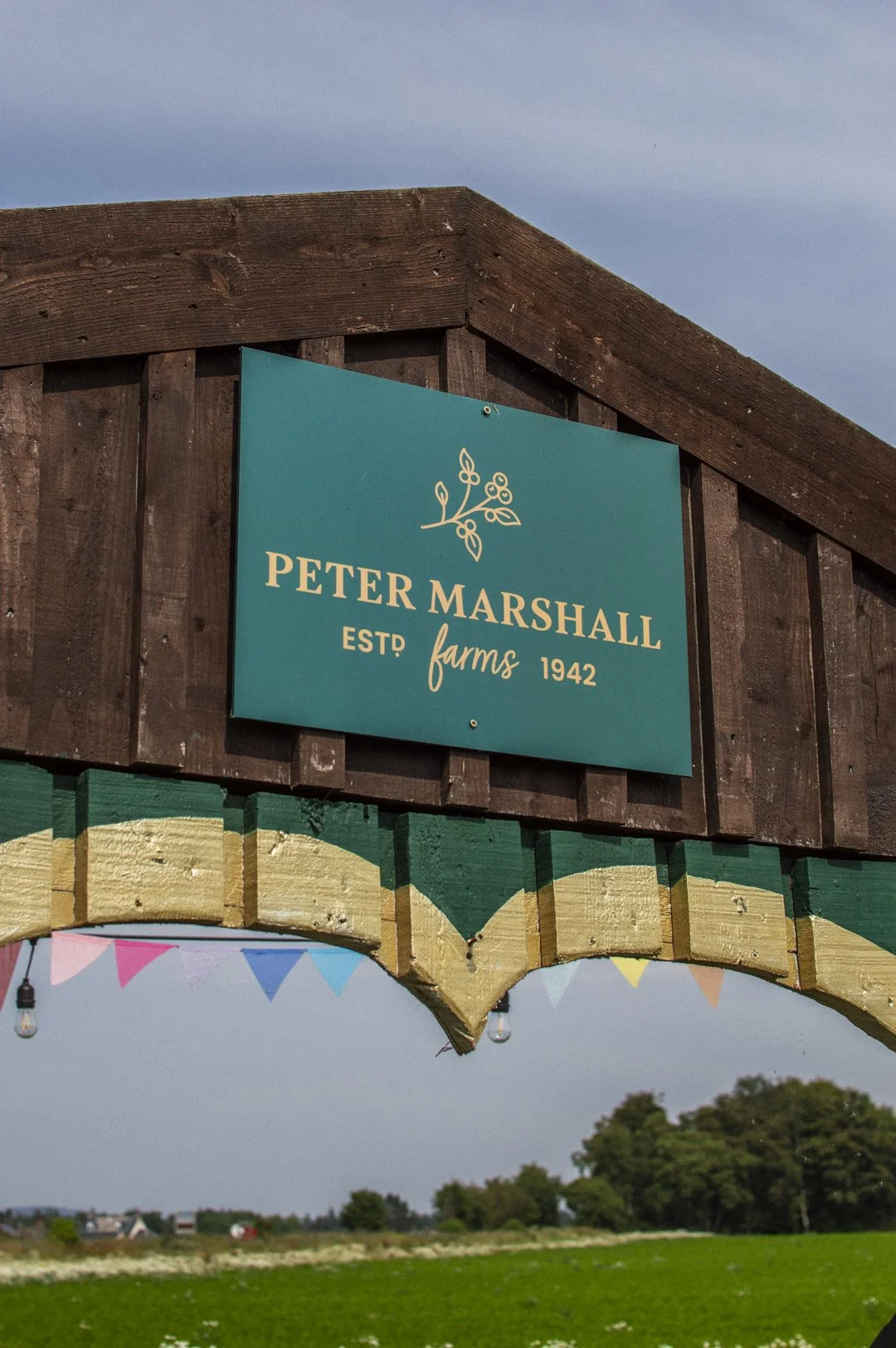 Sign that reads 'Peter Marshall Farms EST 1942' attached to a wooden structure with background of green fields and trees.