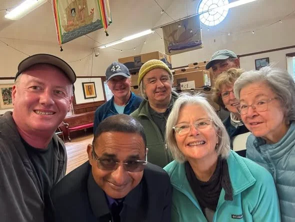 Group of seven people smiling for a selfie in a room with artwork and banners hanging from the ceiling.