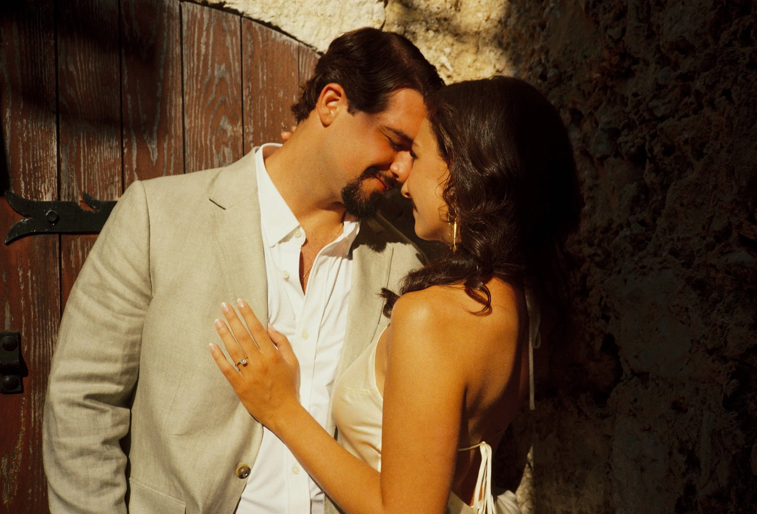 Film photography engagement portrait in the medieval village of Èze on the French Riviera by Cleya Asulon, destination wedding photographer for the Côte d'Azur — couple in an intimate forehead-to-forehead embrace bathed in golden hour sunlight, the m