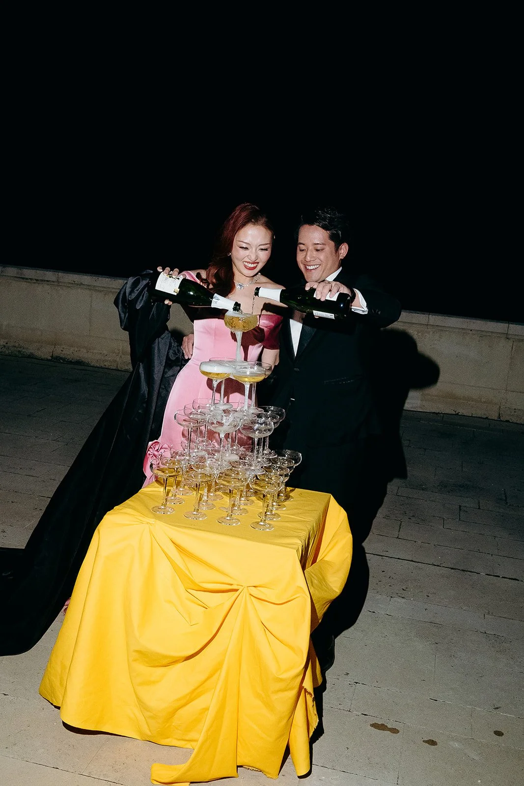 Destination wedding celebration at night, featuring a couple pouring champagne into a glass tower.