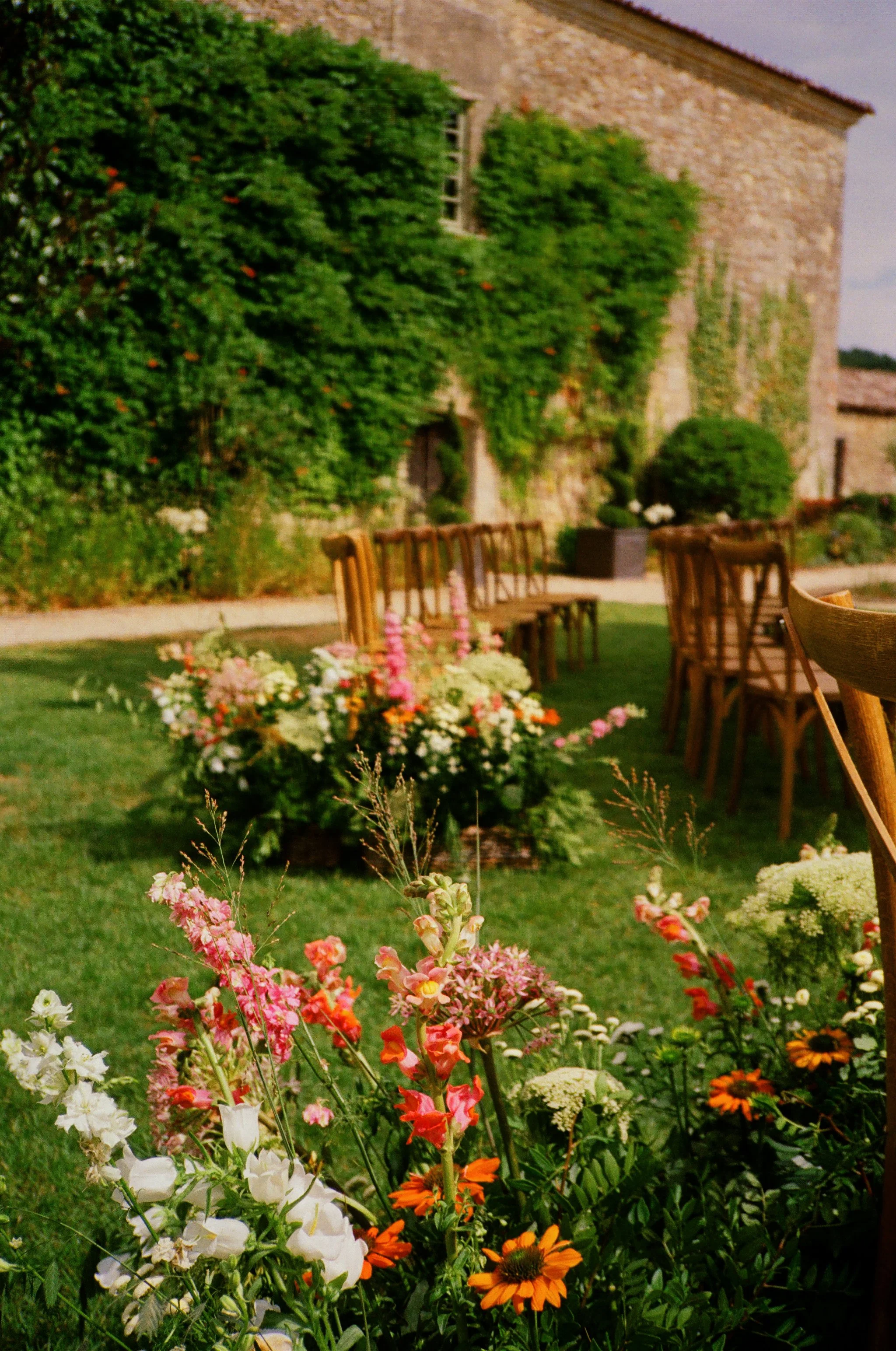 Film photography editorial ceremony setup at Château Rigaud near Bordeaux, France by Cleya Asulon, destination wedding photographer for Bordeaux and the Gironde region — outdoor wedding aisle arranged on a manicured lawn with rows of wooden cross-bac