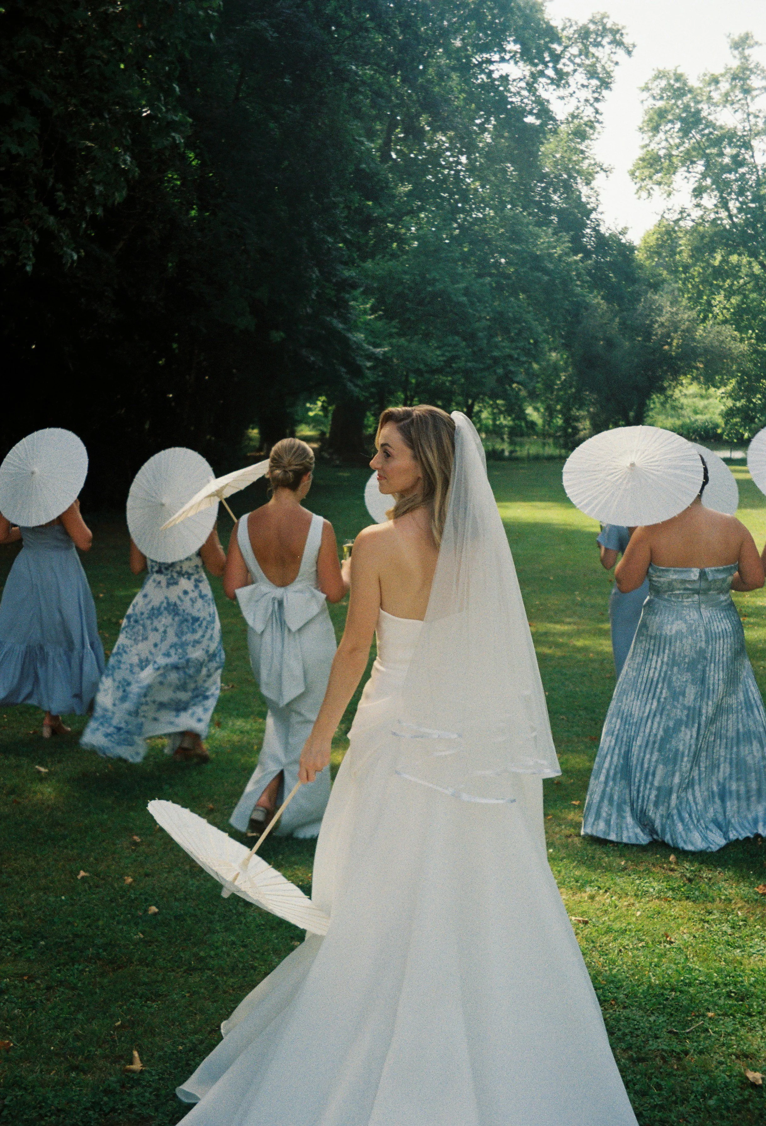 Film photography editorial wedding portrait at a private château near Bordeaux in France by Cleya Asulon, destination wedding photographer for Bordeaux and the Gironde region — bride glancing back over her shoulder while walking through a sunlit lawn