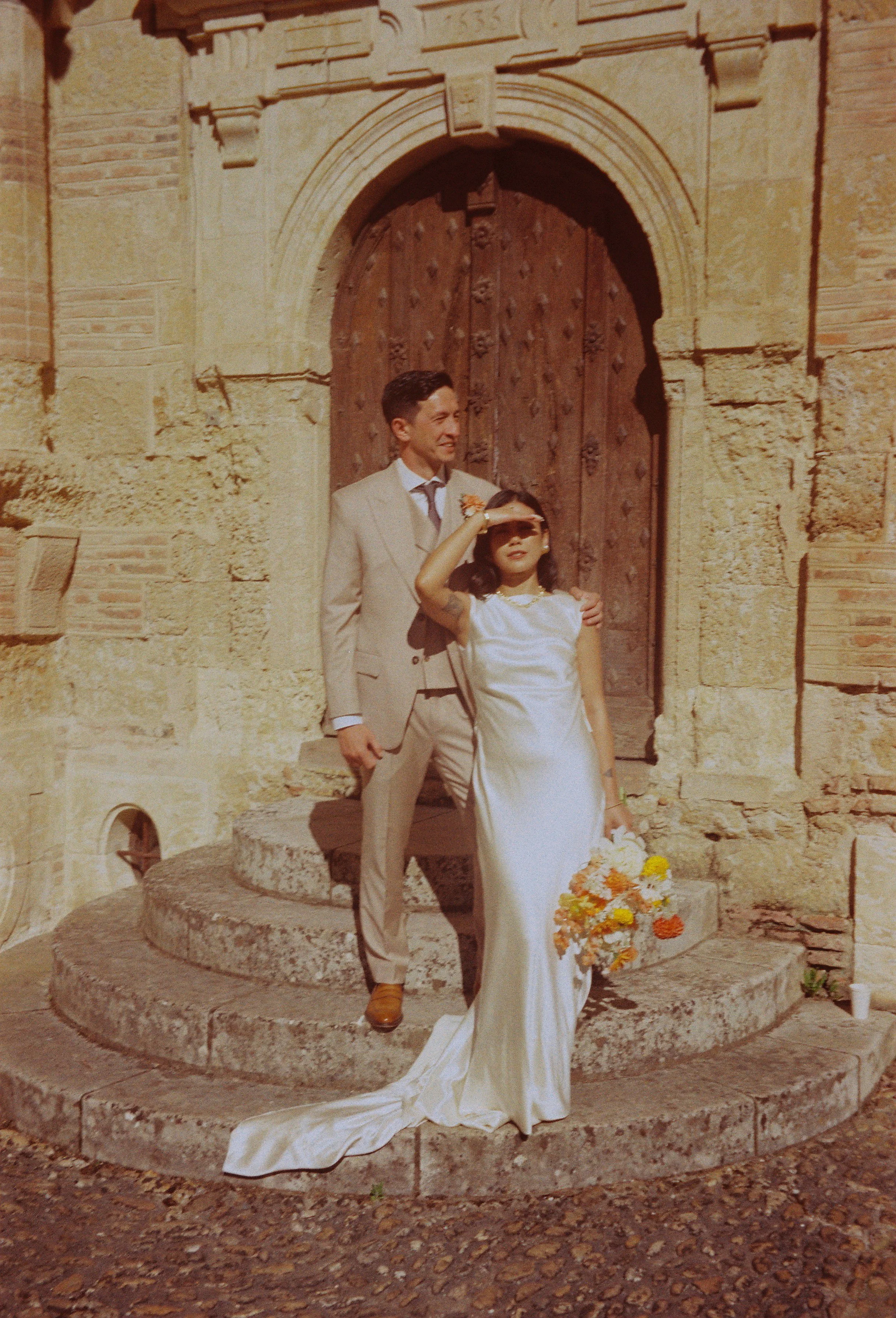 Film photography editorial wedding portrait at a private estate near Toulouse in the South of France by Cleya Asulon, destination wedding photographer for Toulouse and the Occitanie region — bride and groom standing together on the curved stone steps