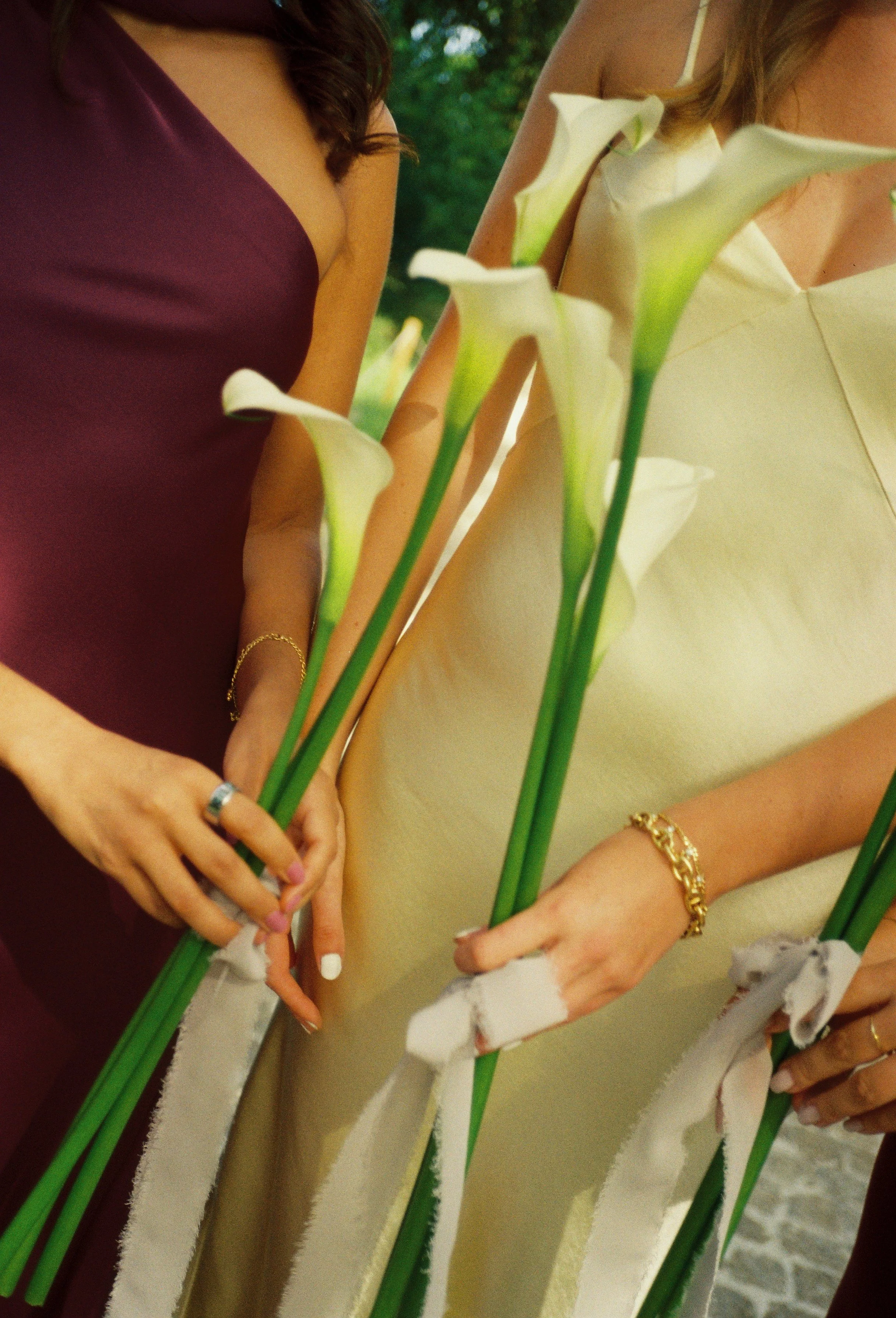 Film photography editorial wedding detail at Château Gassies near Bordeaux, France by Cleya Asulon, destination wedding photographer for Bordeaux and the Gironde region — close-up of two bridesmaids standing side by side in burgundy and champagne sat