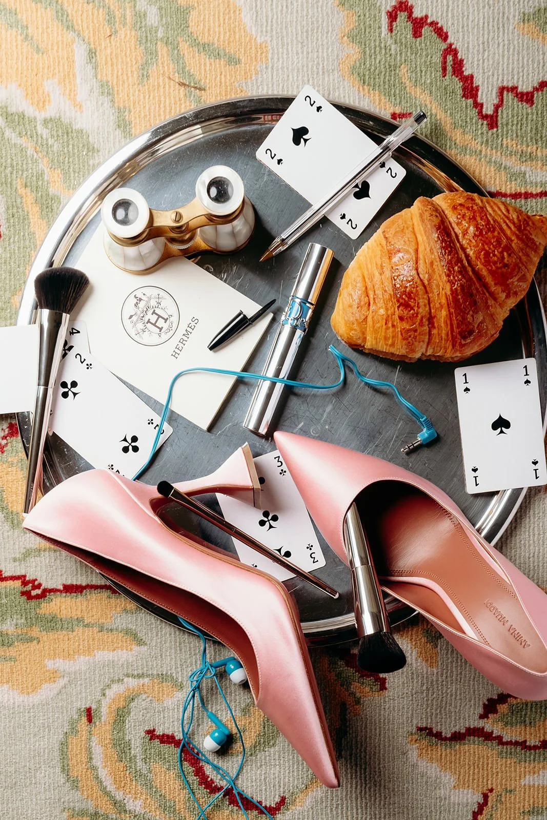 Editorial wedding morning flatlay at Château de Mirambeau (Gironde, France) by Cleya Asulon, destination wedding photographer based in Bordeaux and Cognac — silver tray styled on a vintage floral patterned rug featuring Aminah Muaddi pink satin pumps