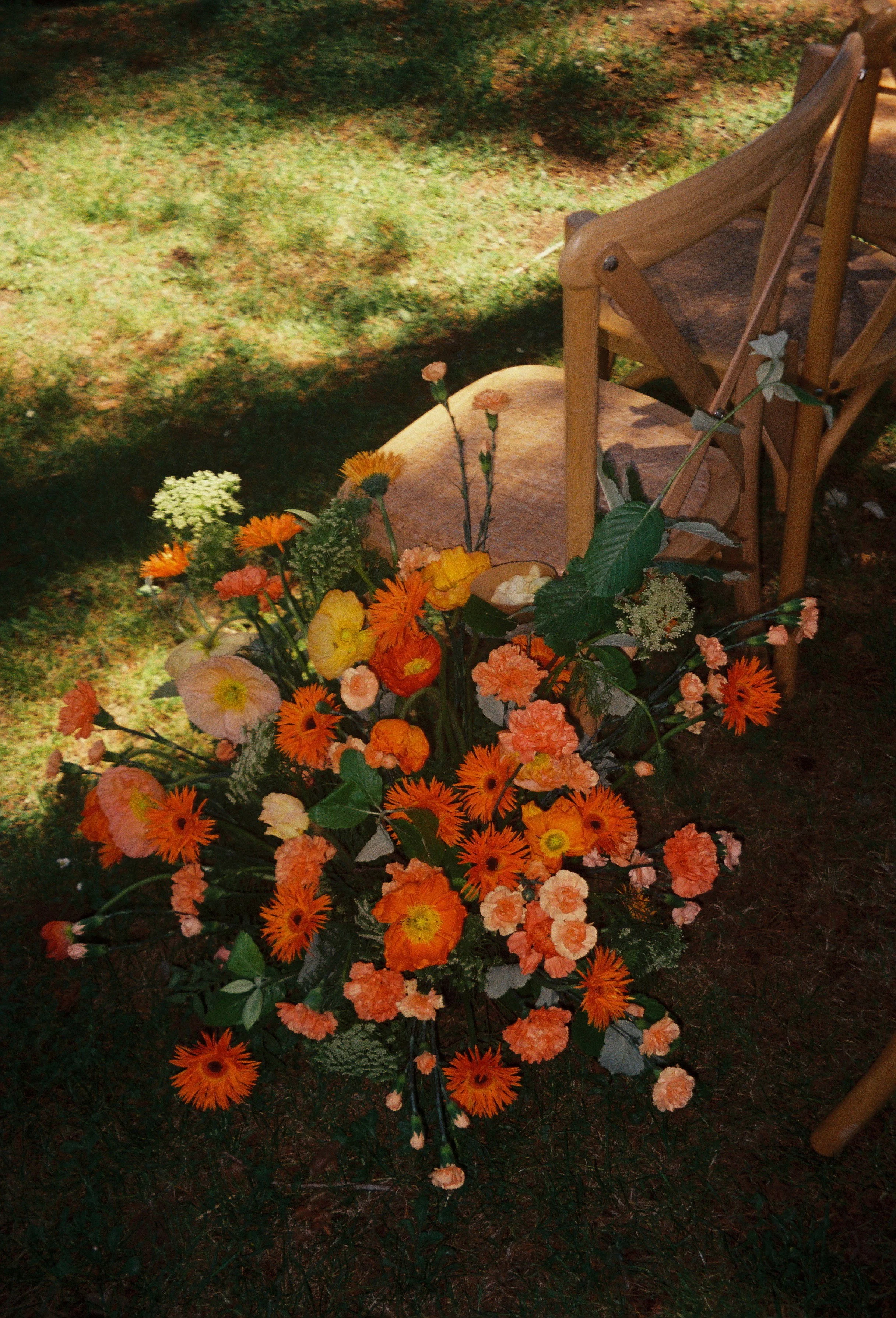 Film photography editorial wedding ceremony floral detail at a private estate near Toulouse in the South of France by Cleya Asulon, destination wedding photographer for Toulouse and the Occitanie region — close-up of a vibrant ground floral arrangeme