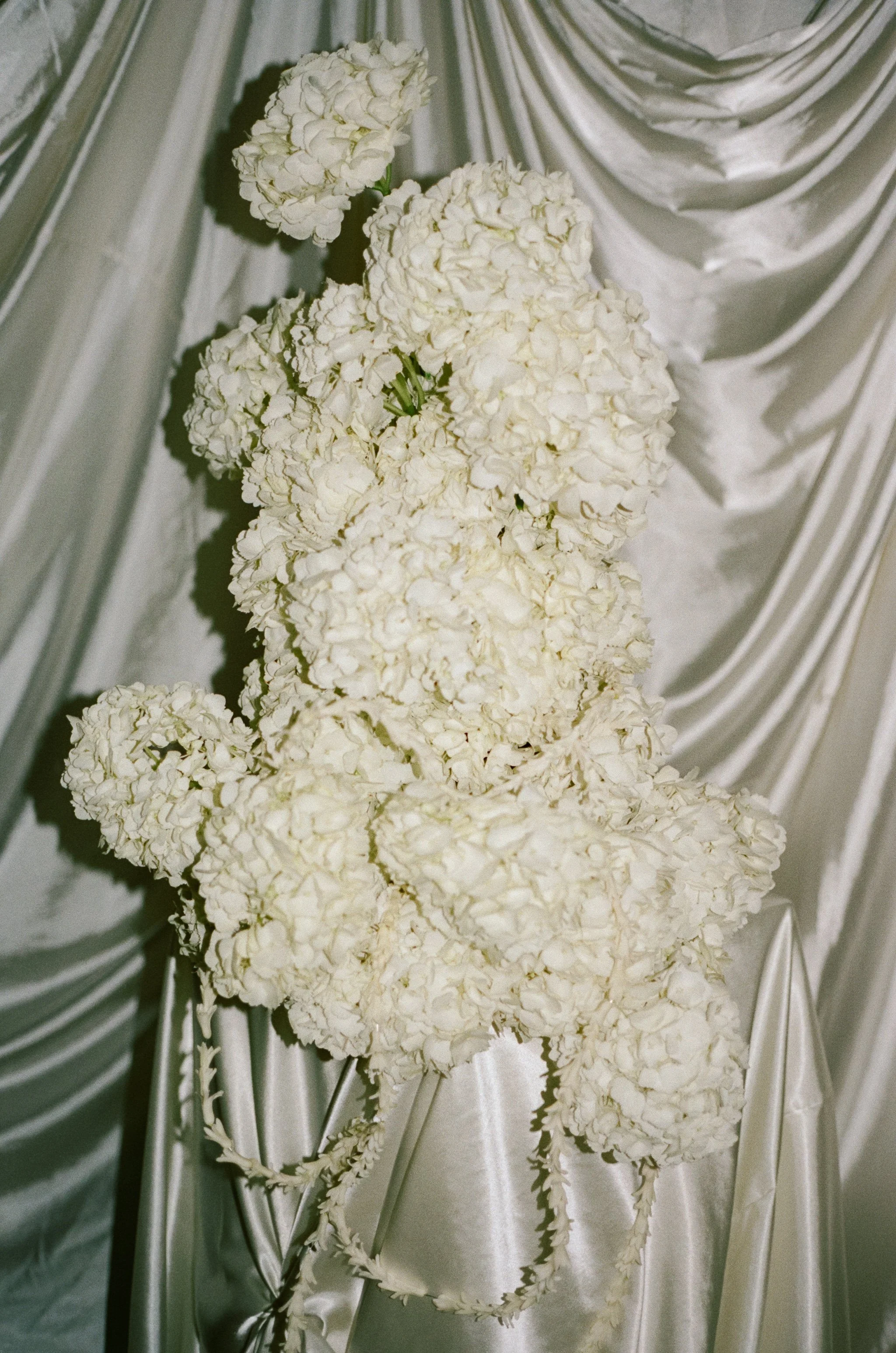 White floral arrangement with large hydrangea blooms on a satin-covered table, with satin draped background.