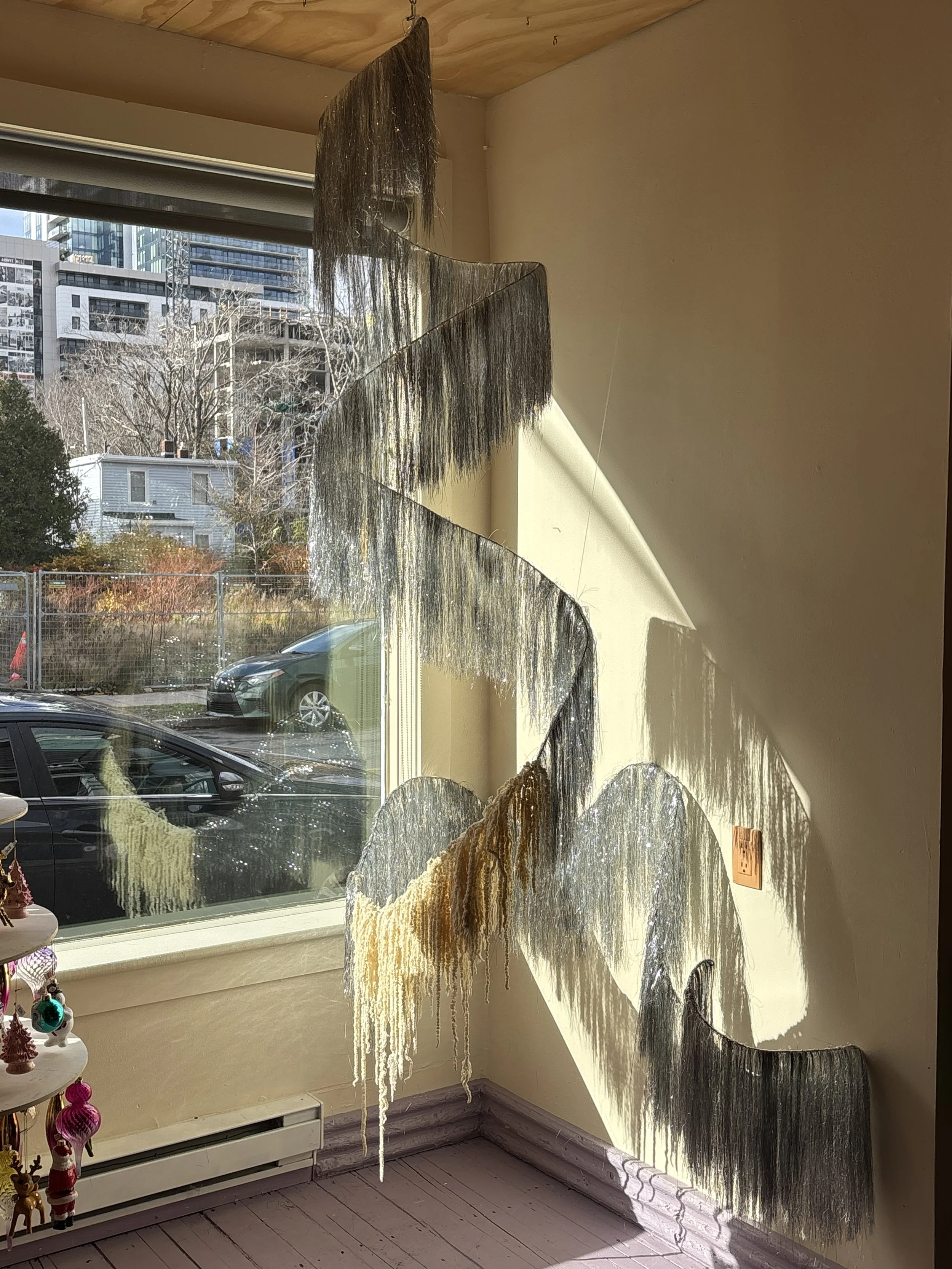 Colorful woven wall hanging art piece casting shadows on the wall near a window.