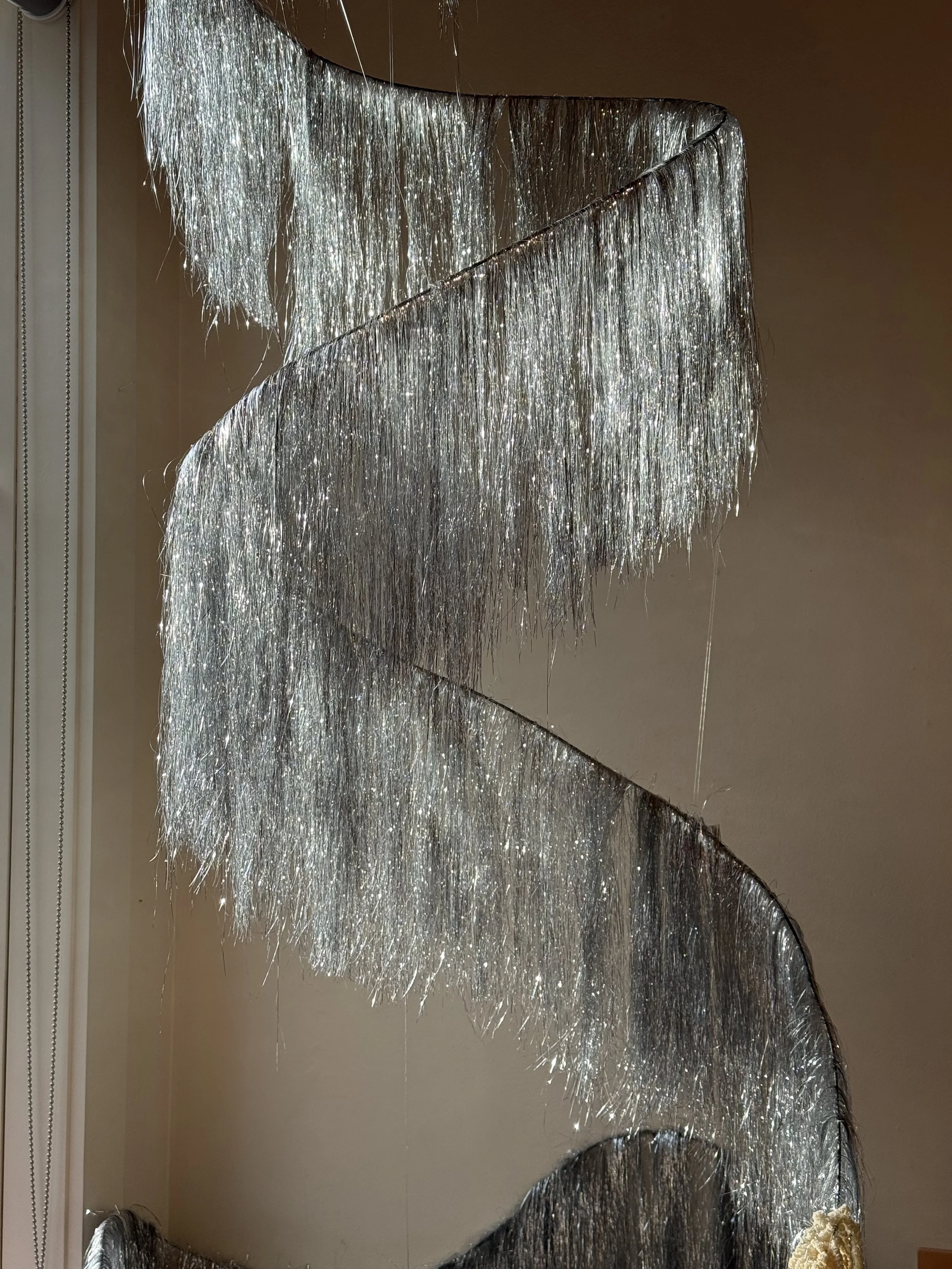 A decorative spiral chandelier made of silver metallic hanging strands that reflect light.