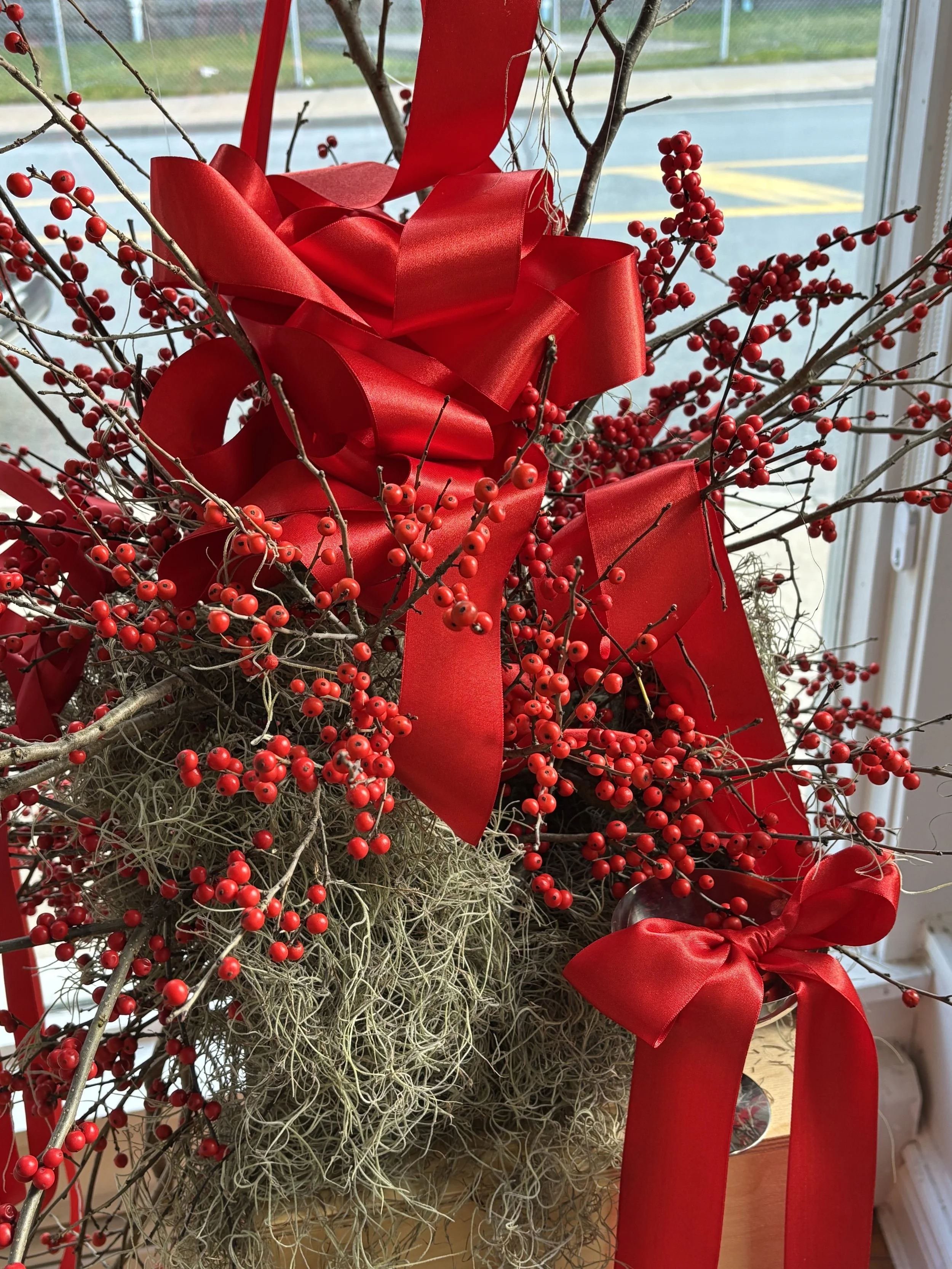 Decorative holiday arrangement featuring red berries, large red ribbons, and dried moss, placed indoors near a window.