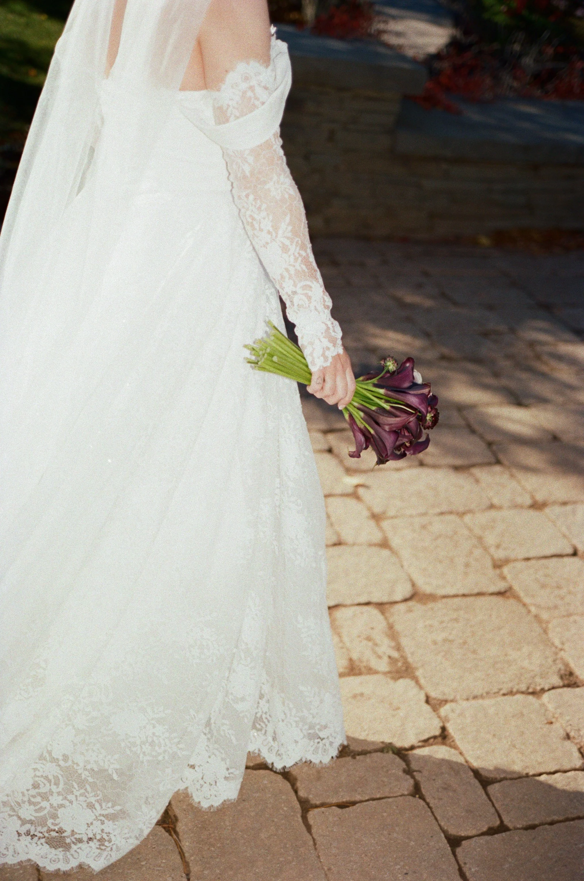Bride in a white lace wedding dress holding a bouquet of dark purple calla lilies.