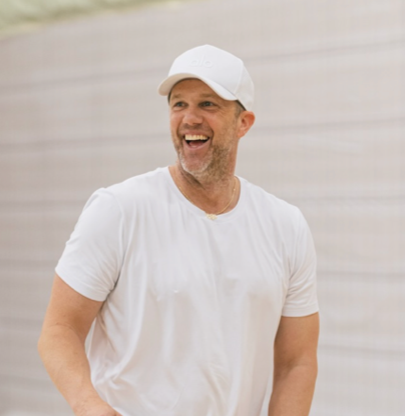 A smiling man wearing a white baseball cap and white t-shirt.