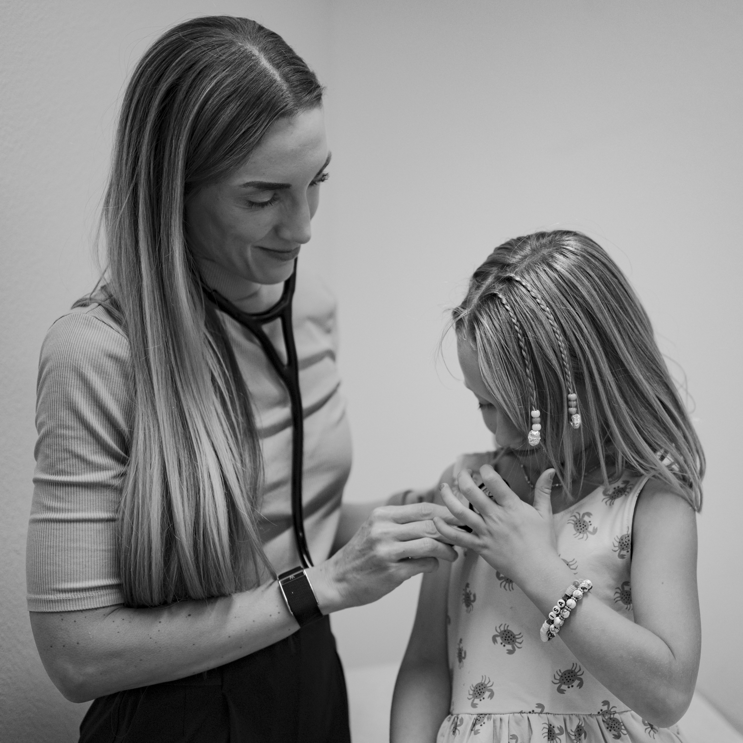 Dr. Erica Strandberg, DO examining a young girl. Dr. Strandberg is smiling and gently holding the girl's hand during the check-up.