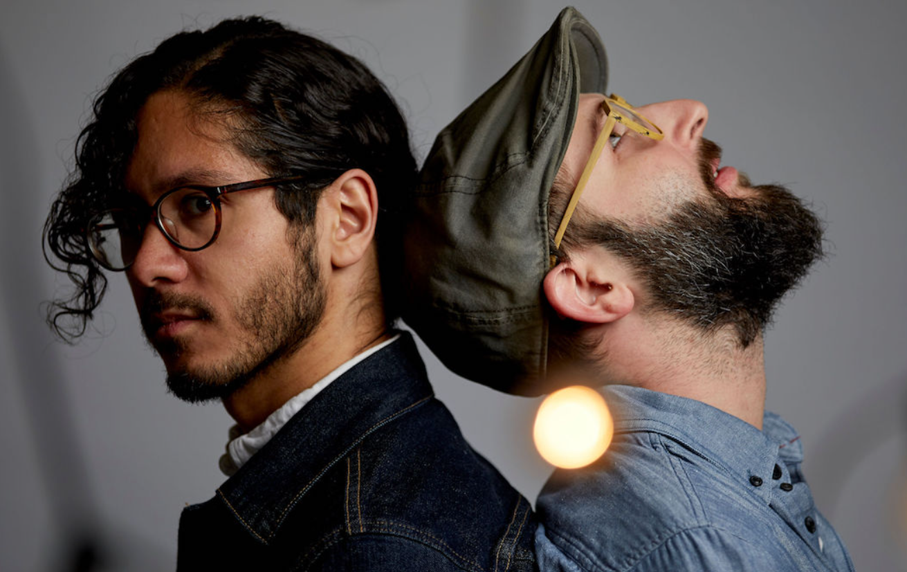 Two men each with eyeglasses, standing back to back .