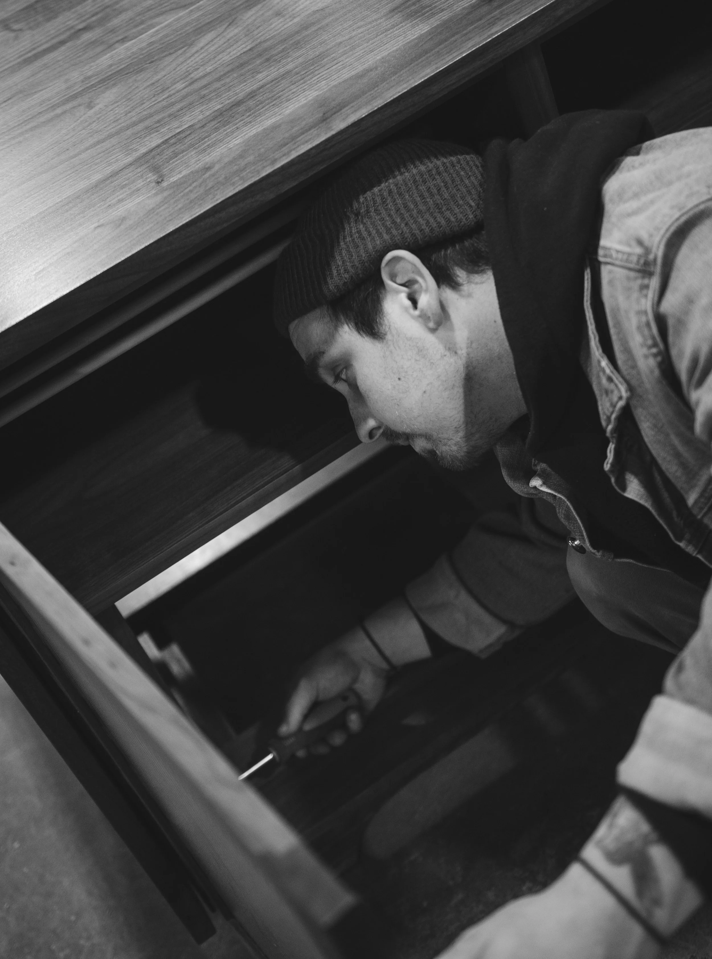 A man working inside a wooden cabinet, using a screwdriver.