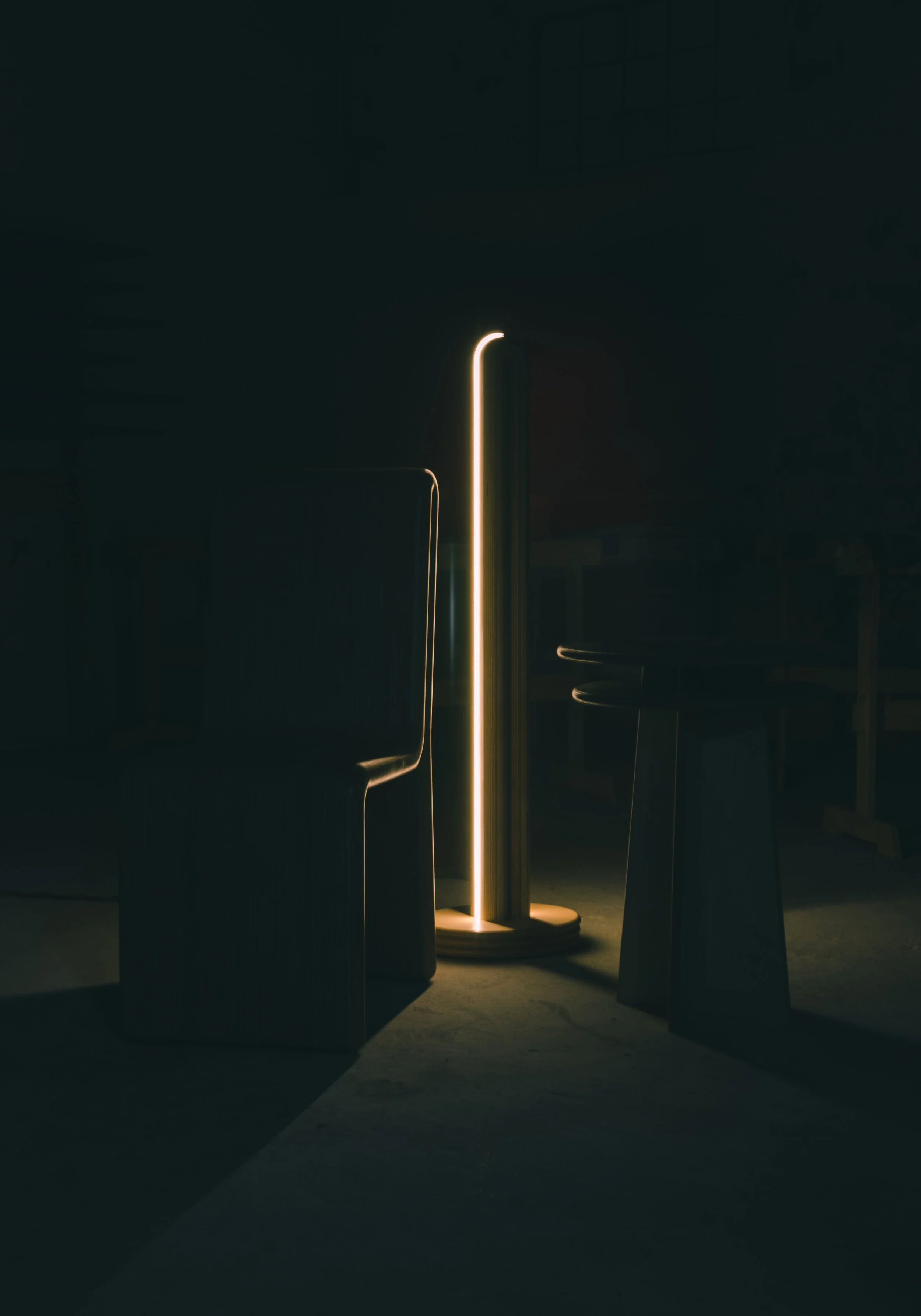 Dimly lit room with a modern floor lamp emitting warm light, surrounded by dark chairs and furniture.