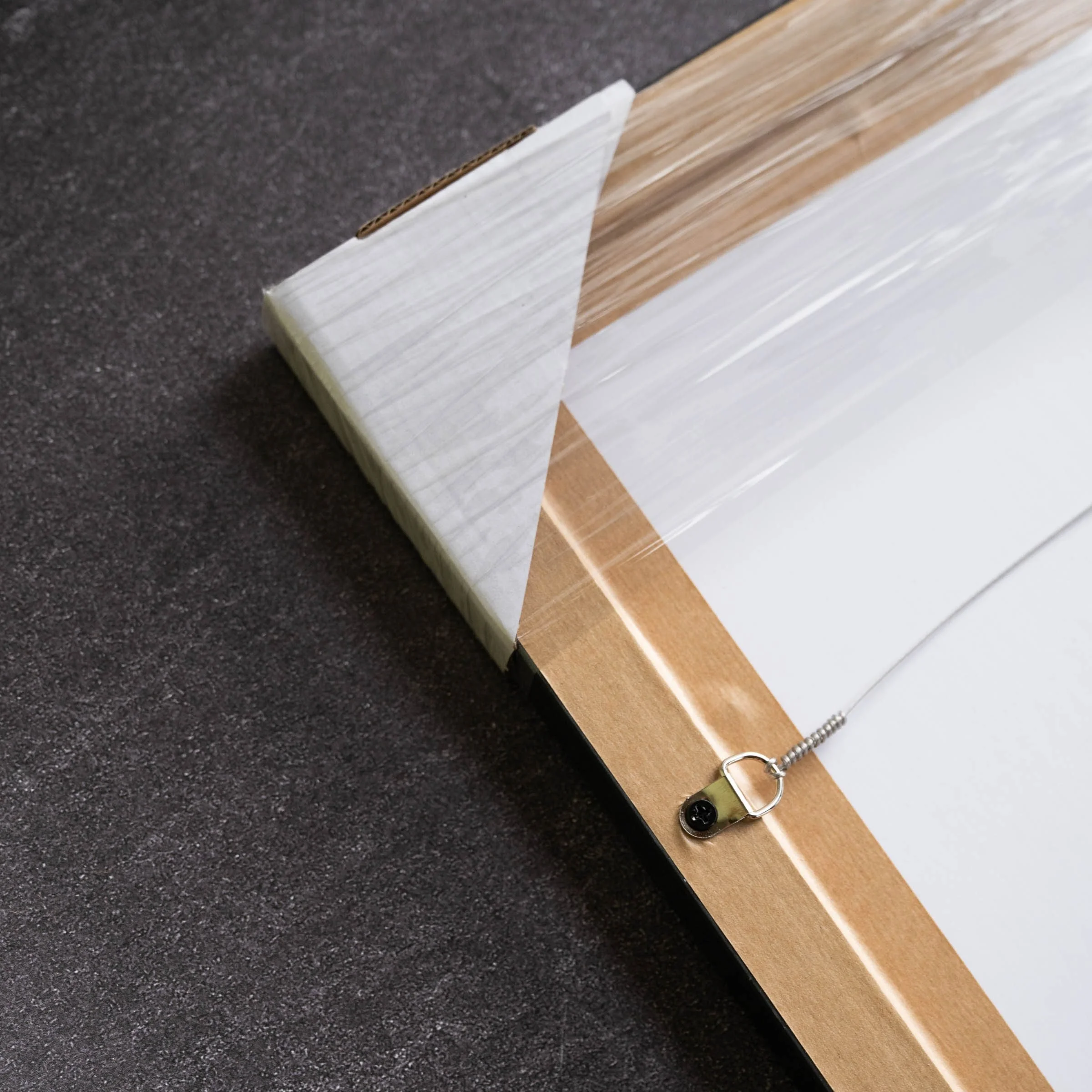 Framed print corner showing raw oak finish and wall-mount hanging wire, ready for shipping