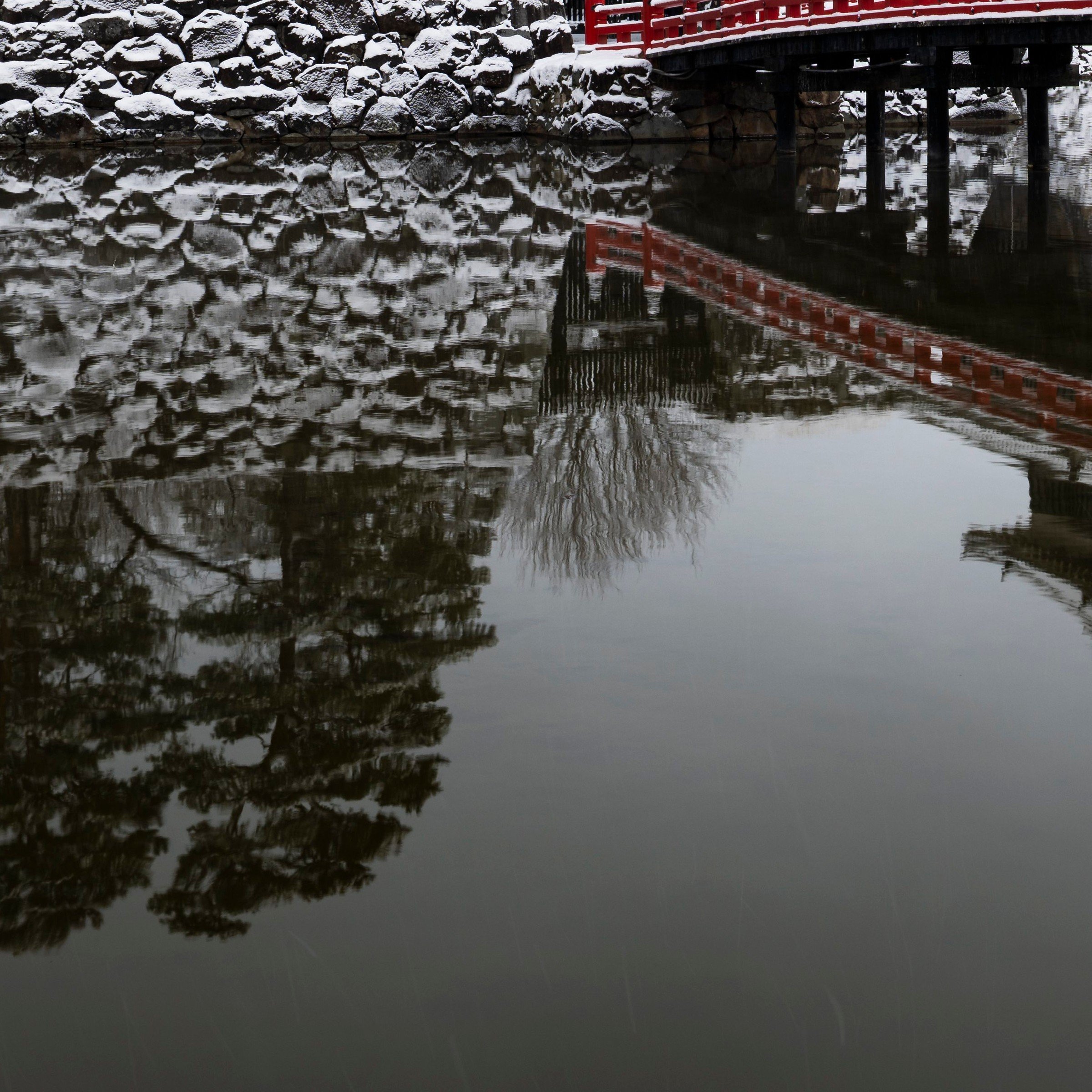 Close-up of the red bridge at Matsumoto Castle reflected in the snow-covered moat, Nagano Prefecture, Japan