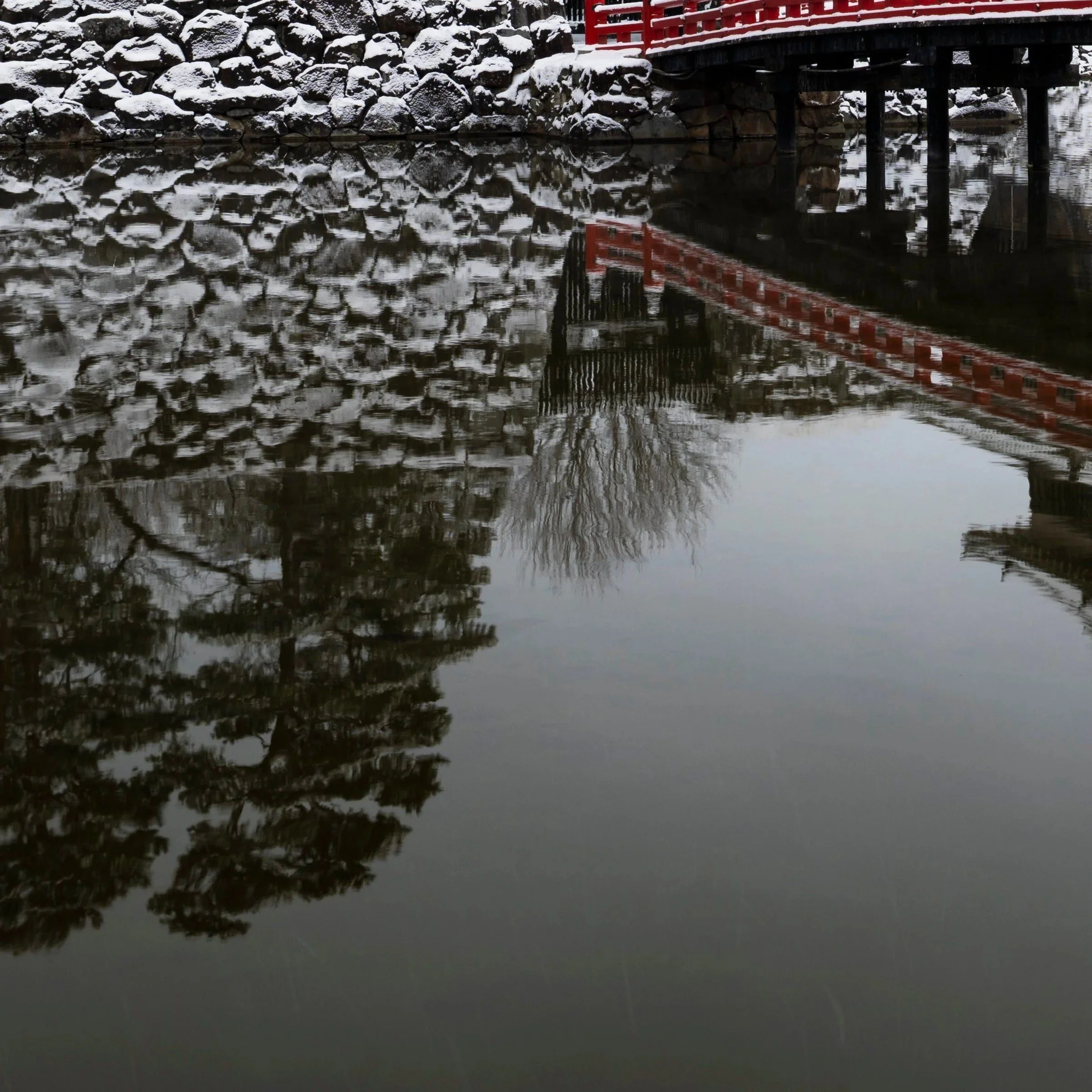 Close-up of the red bridge at Matsumoto Castle reflected in the snow-covered moat, Nagano Prefecture, Japan