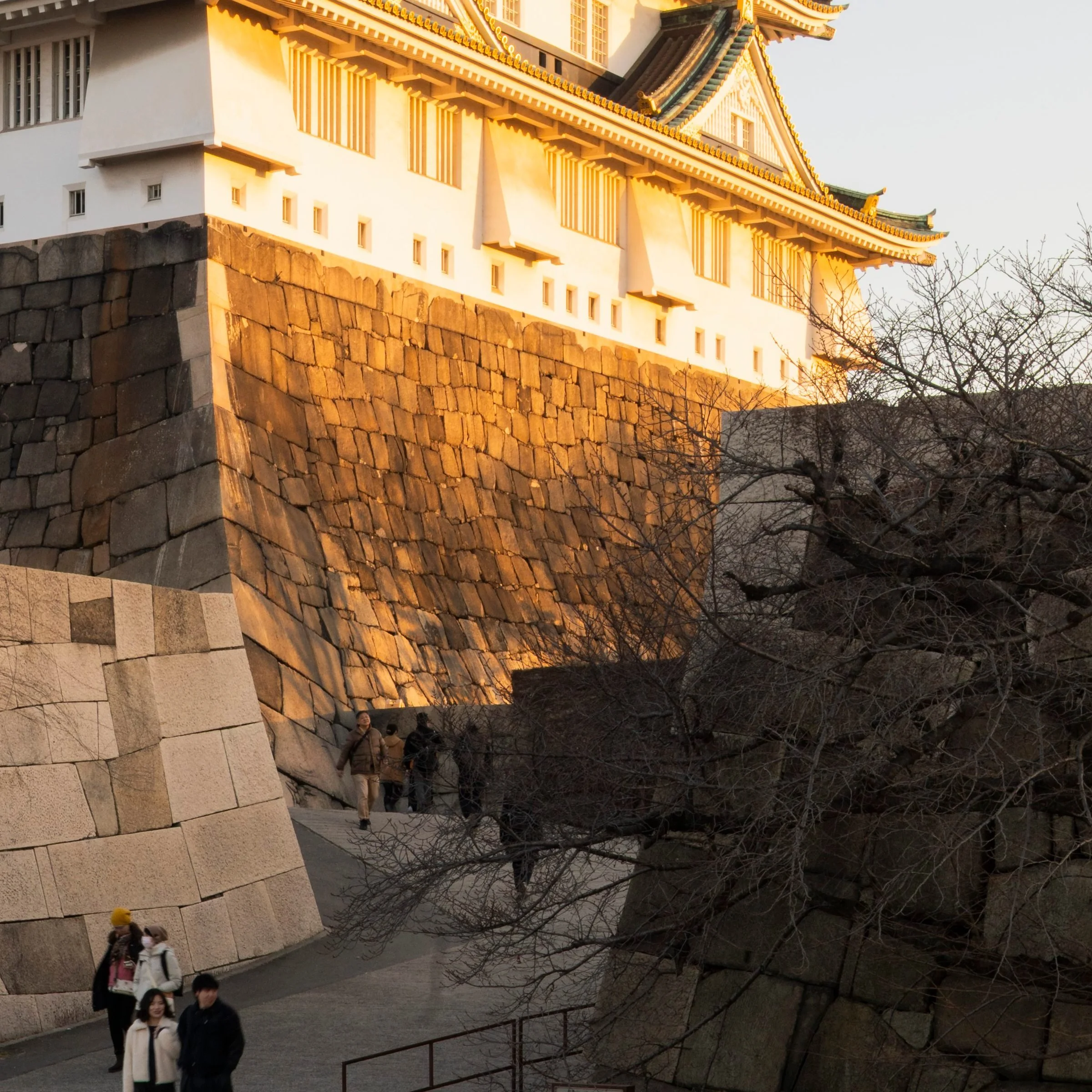 Visitors dwarfed by the castle ramparts at golden hour, Osaka, Japan