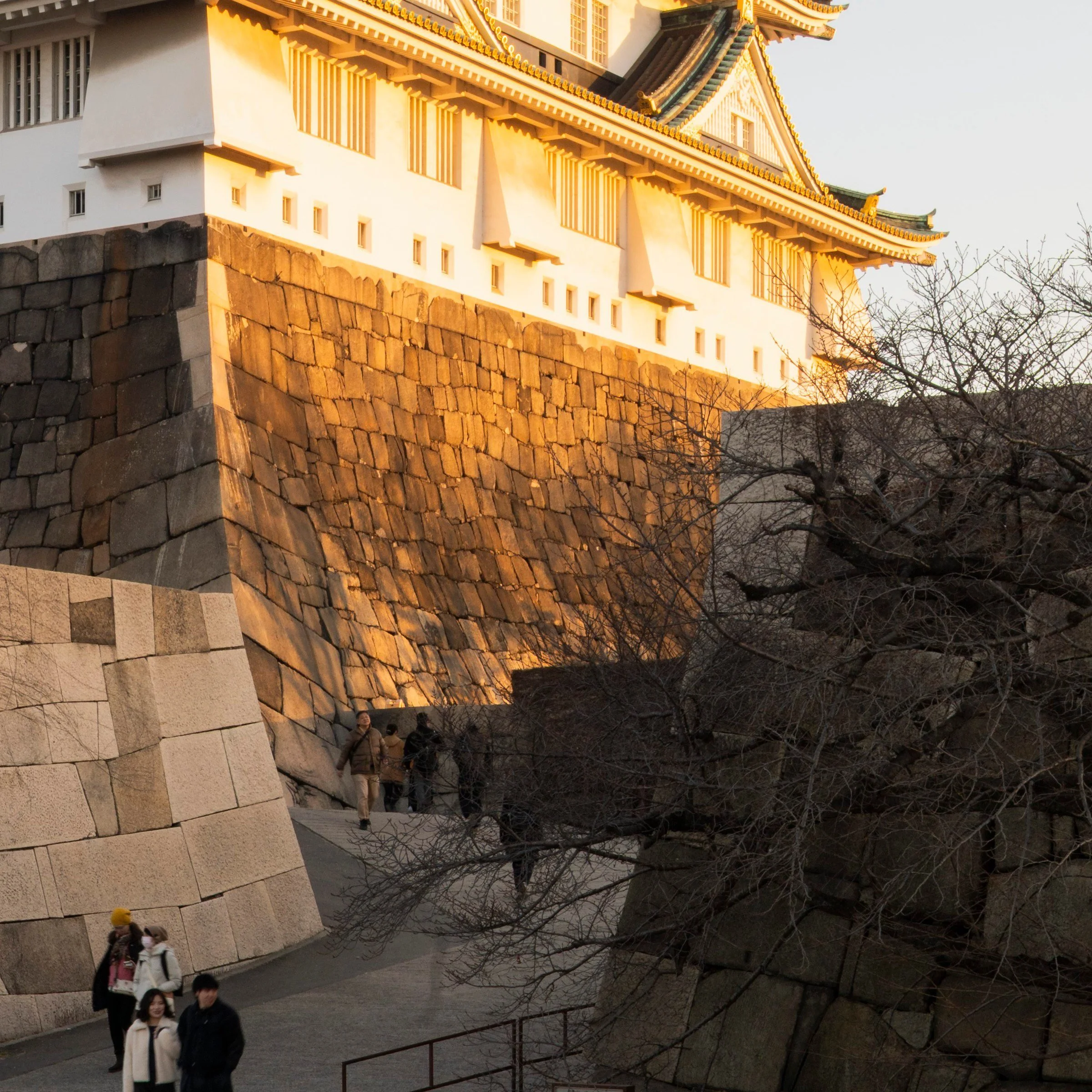 Visitors dwarfed by the castle ramparts at golden hour, Osaka, Japan
