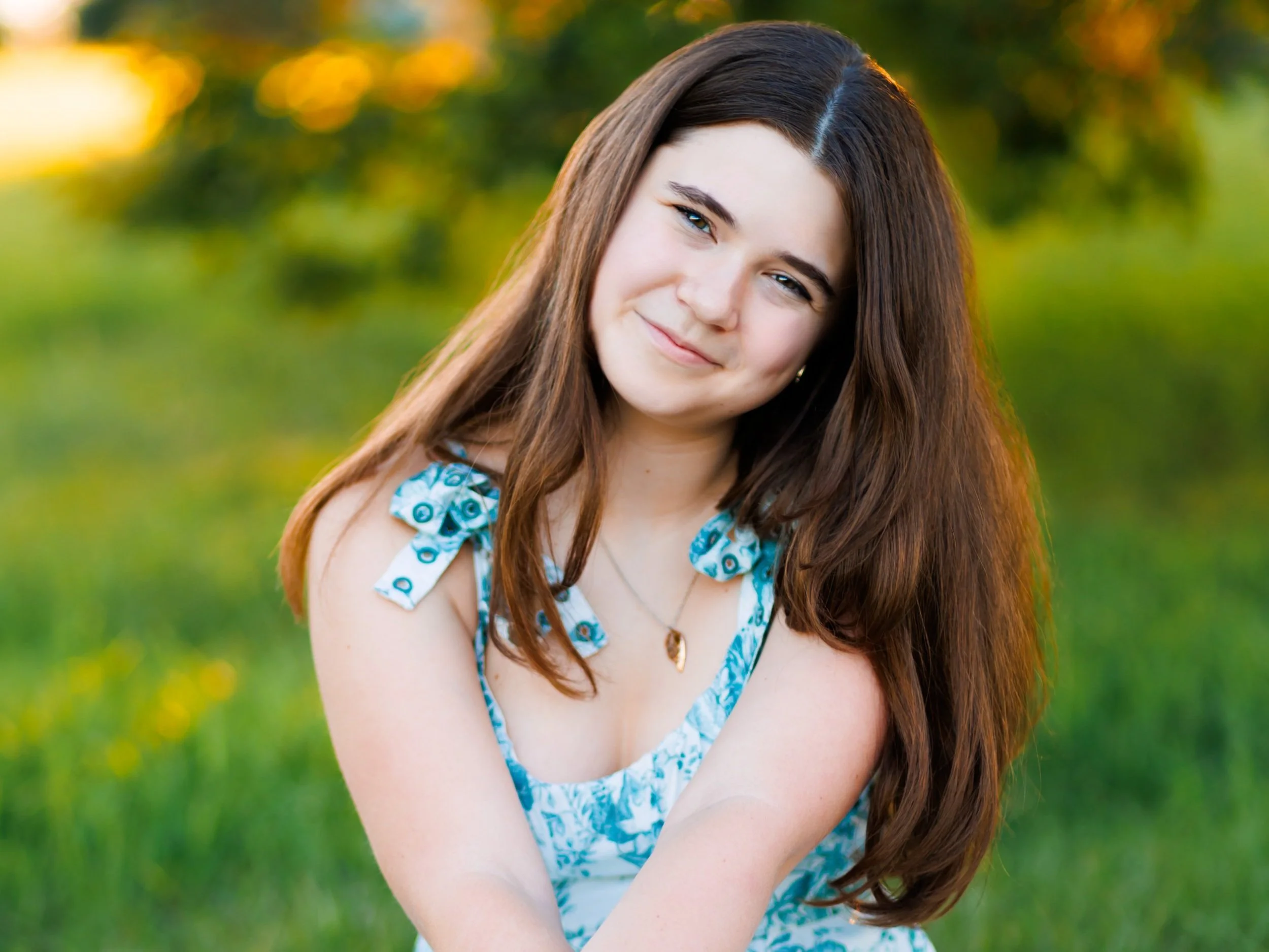 senior photo of a girl with a blue floral dress sitting in the grass in Gretna, NE