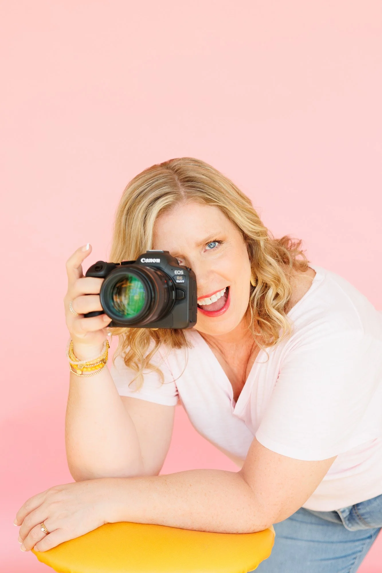 Headshot of woman with camera on pink backdrop