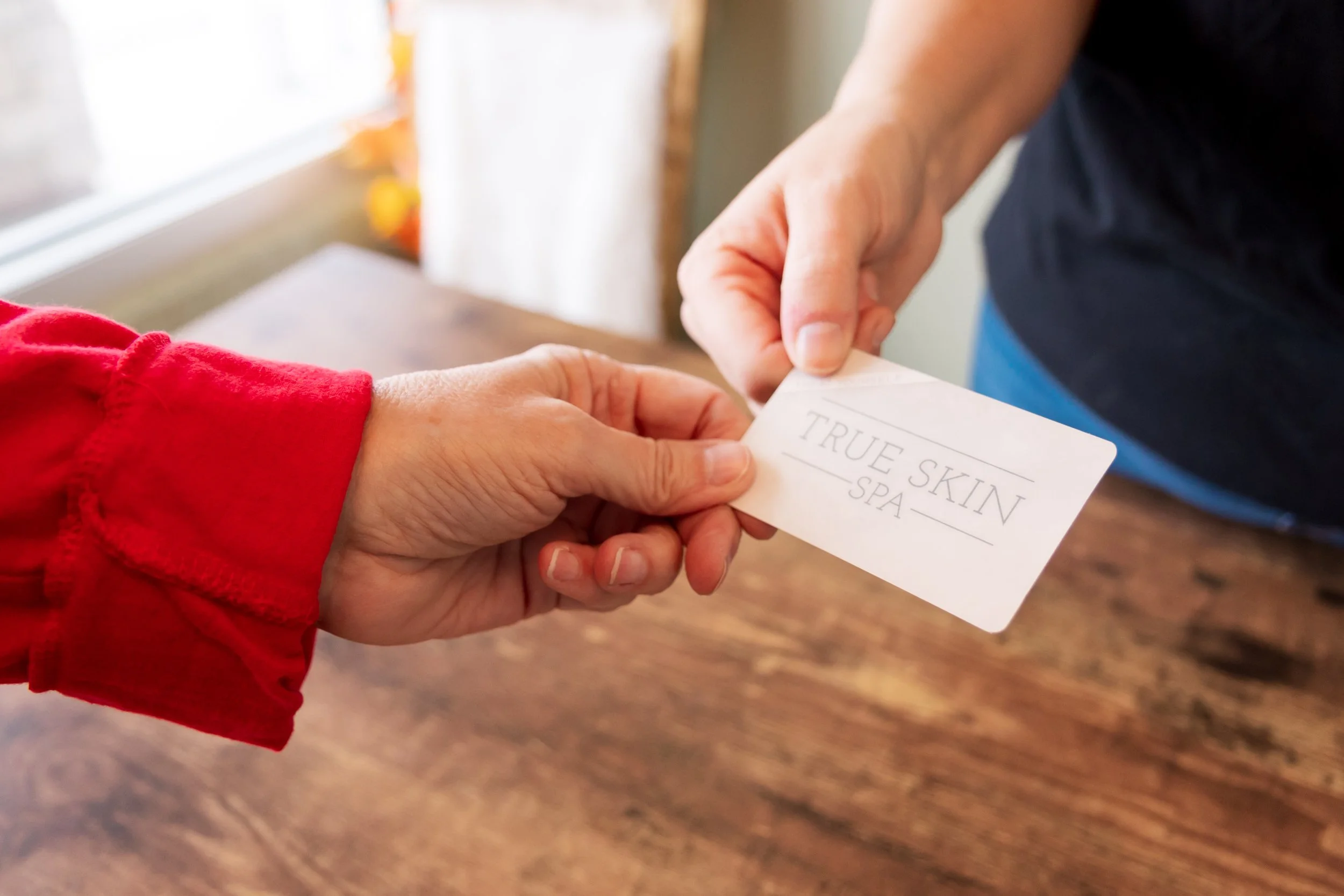closeup photo of a woman handing another woman a business card from True Skin Spa