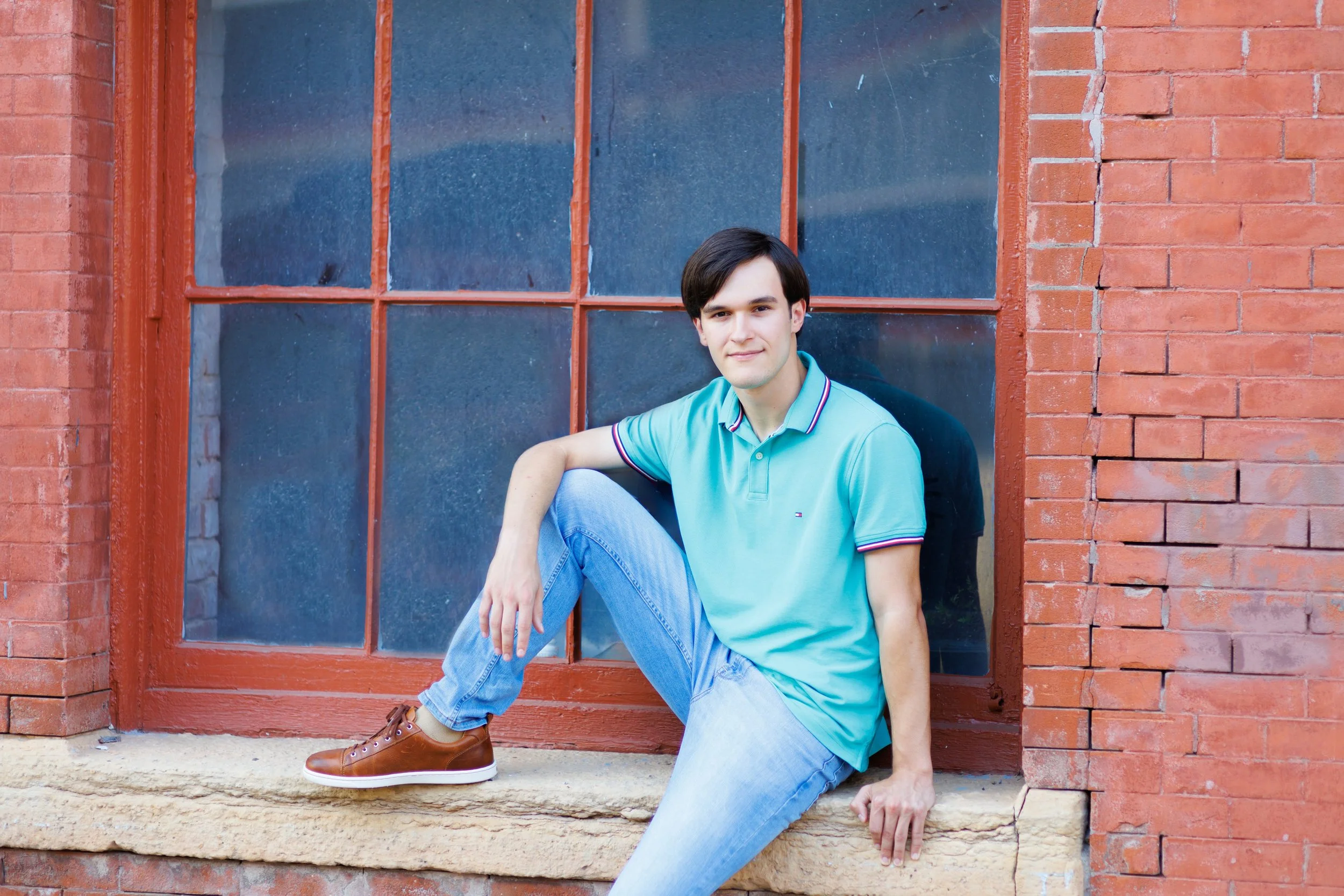 senior photo of a boy sitting in a window of an old brick building