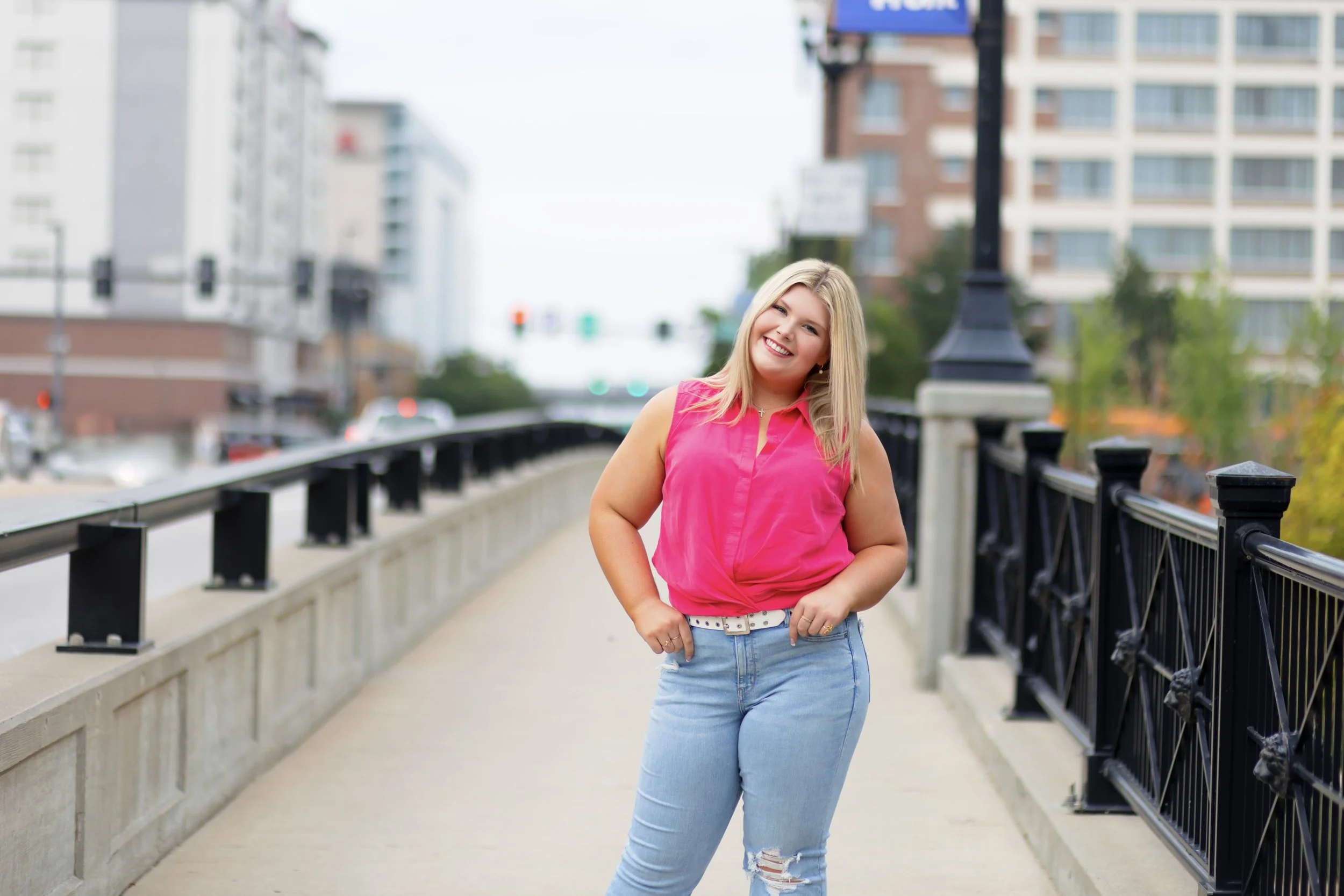 senior photo of a girl in a pink top and jeans on a bridge