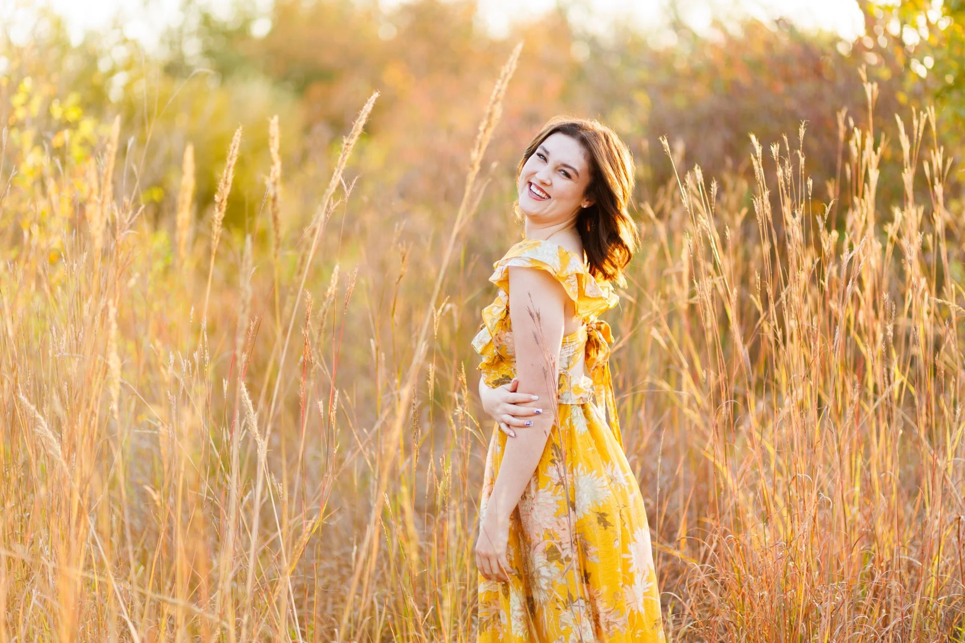 senior photo of a girl in a yellow dress laughing in golden tall grass