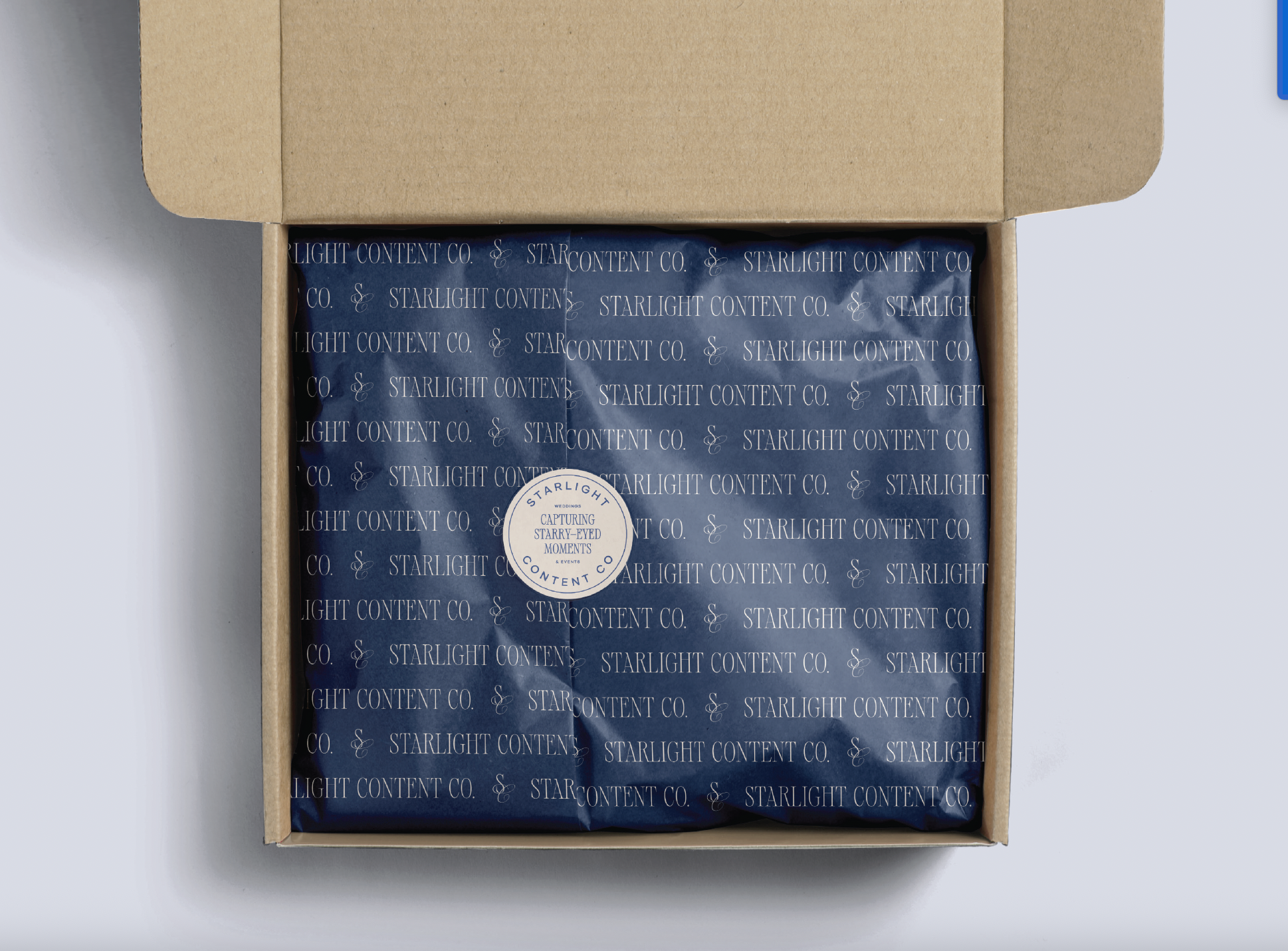 Open cardboard box containing wrapped item with blue patterned paper and a circular label reading "StarLight Content Co. capturing starry-eyed moments"