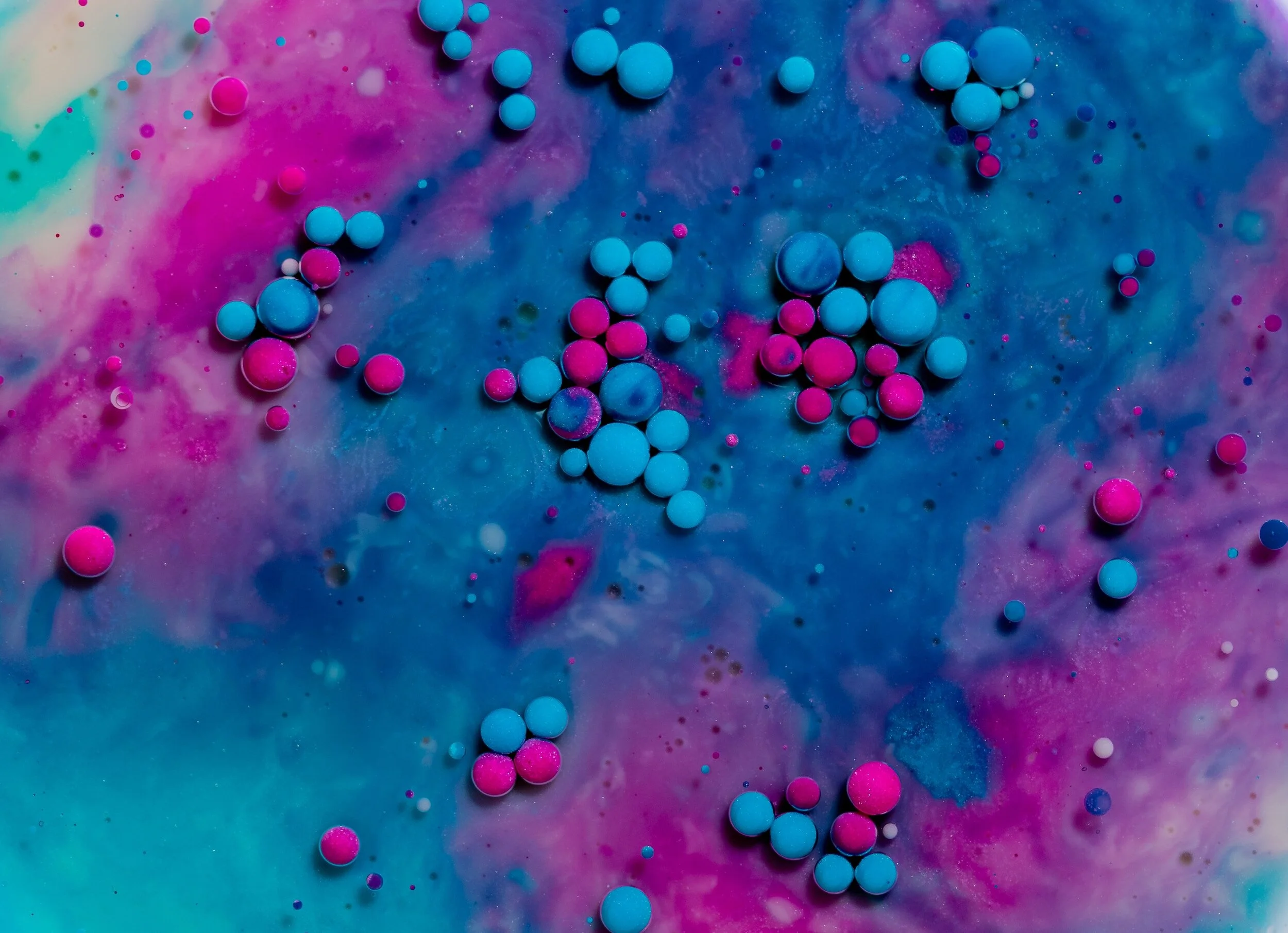 An abstract art image. Small blue and pink spheres clump together on a blue and pink swirled liquid background.