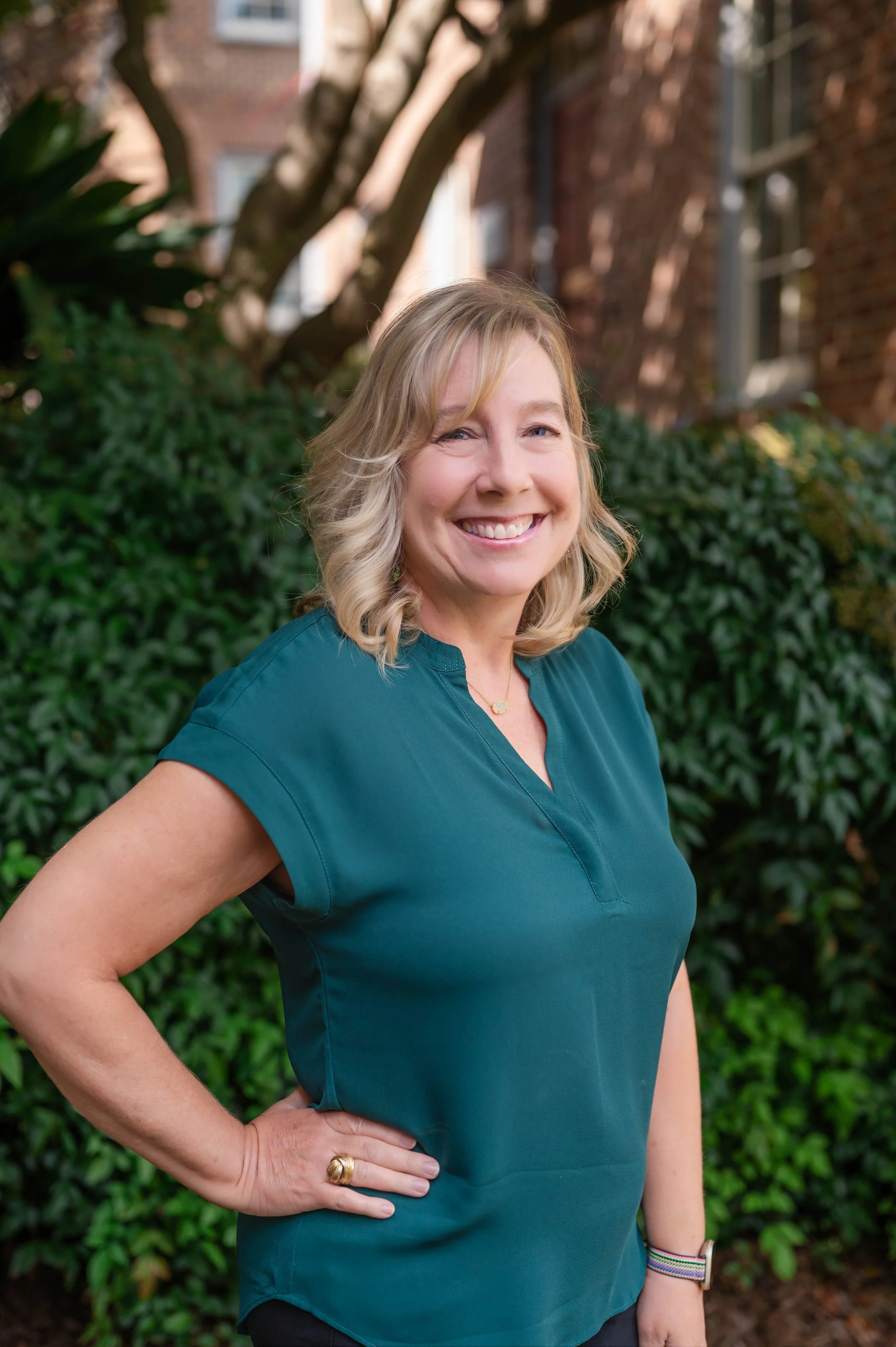 Woman in green shirt smiling outdoors with greenery in background