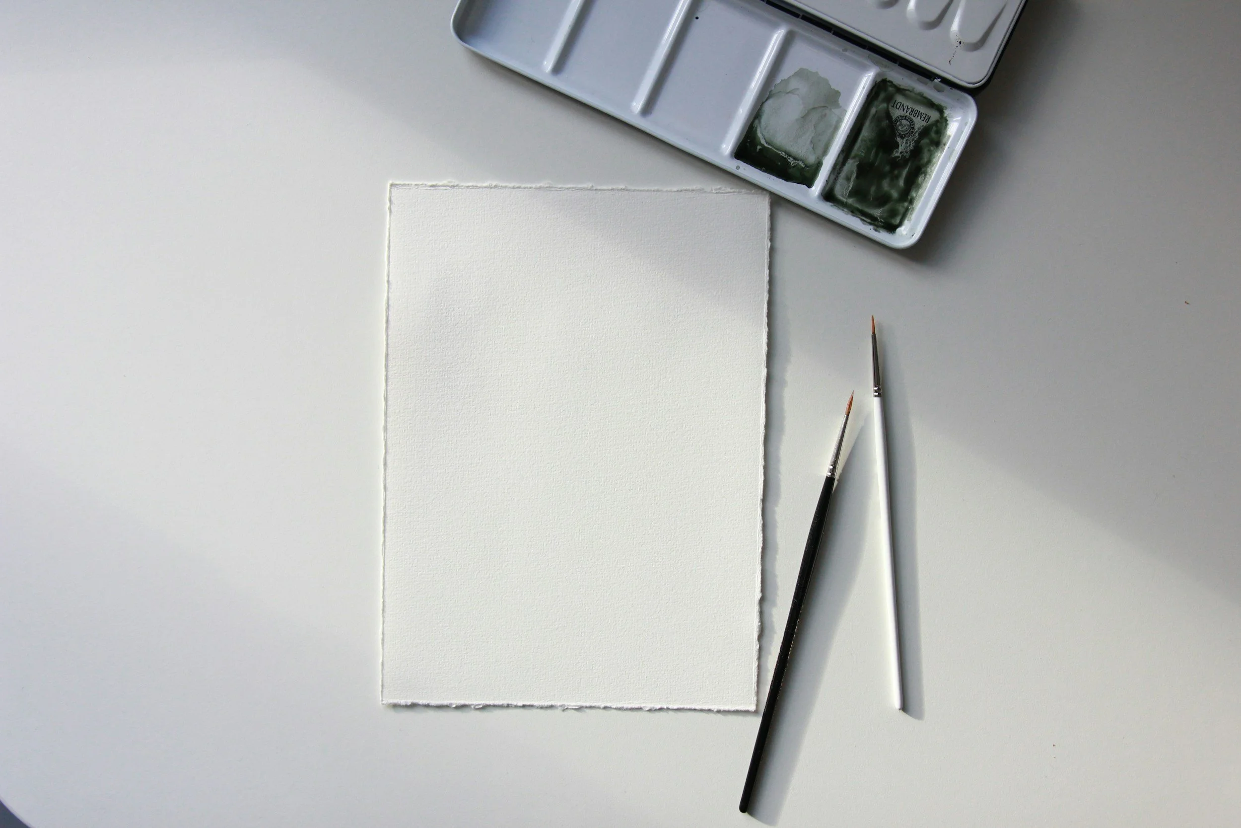 Blank white paper on a studio table surrounded by watercolor paints and brush, representing art therapy services in Maryland, Washington DC, and Missouri.