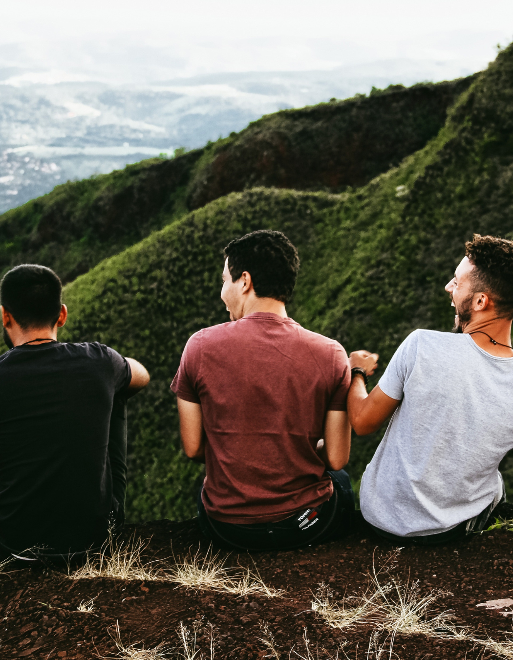 Three adult men sitting together outside engaged in a supportive group conversation.