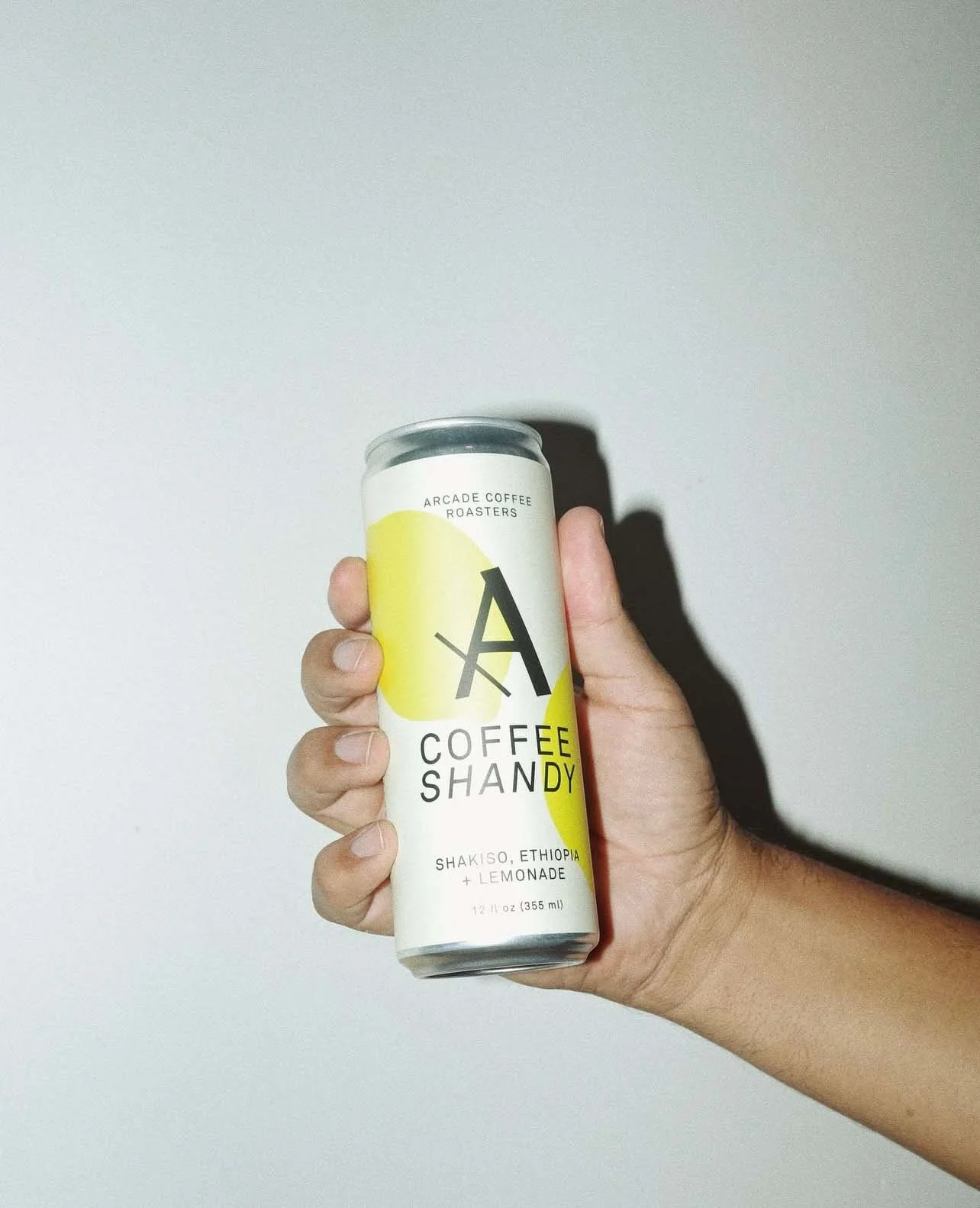 Hand holding a can of Arcade Coffee Roasters Shakiso Ethiopia Lemonade coffee drink against a plain wall.
