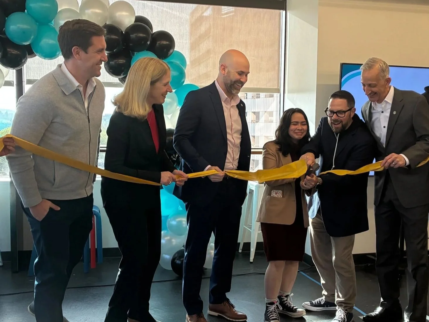 Group of people celebrating a ribbon-cutting ceremony with balloons in the background.