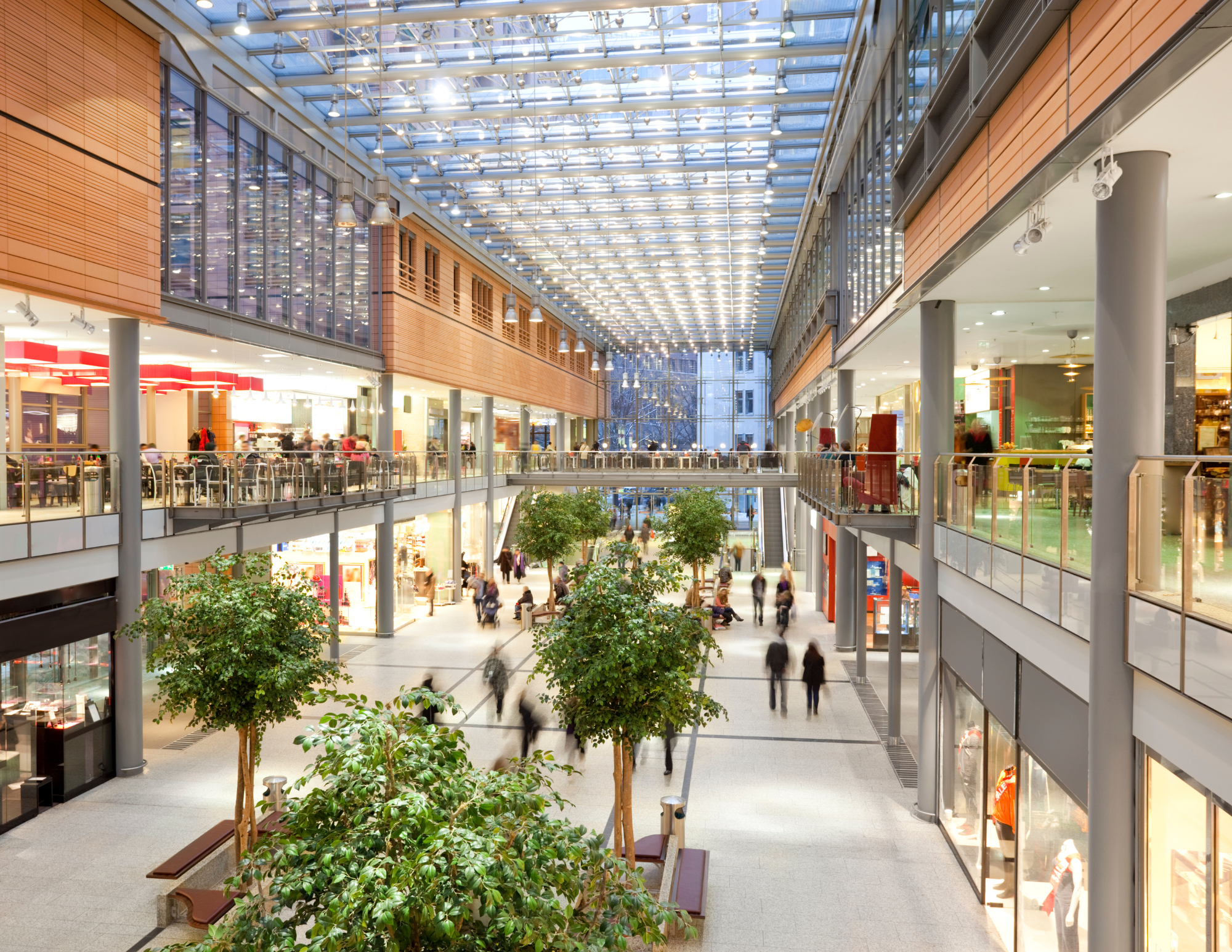 Image depicts a shopping mall with two floors of stores. The people on the main floor are caught in motion walking
