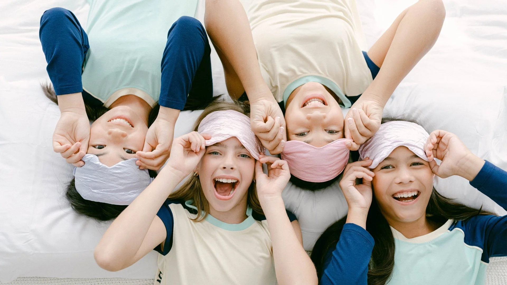 This is an image from ARD's client, The Decided Collection, where four tween girls are laying on a pillow with sleep masks looking up at the camera and smiling