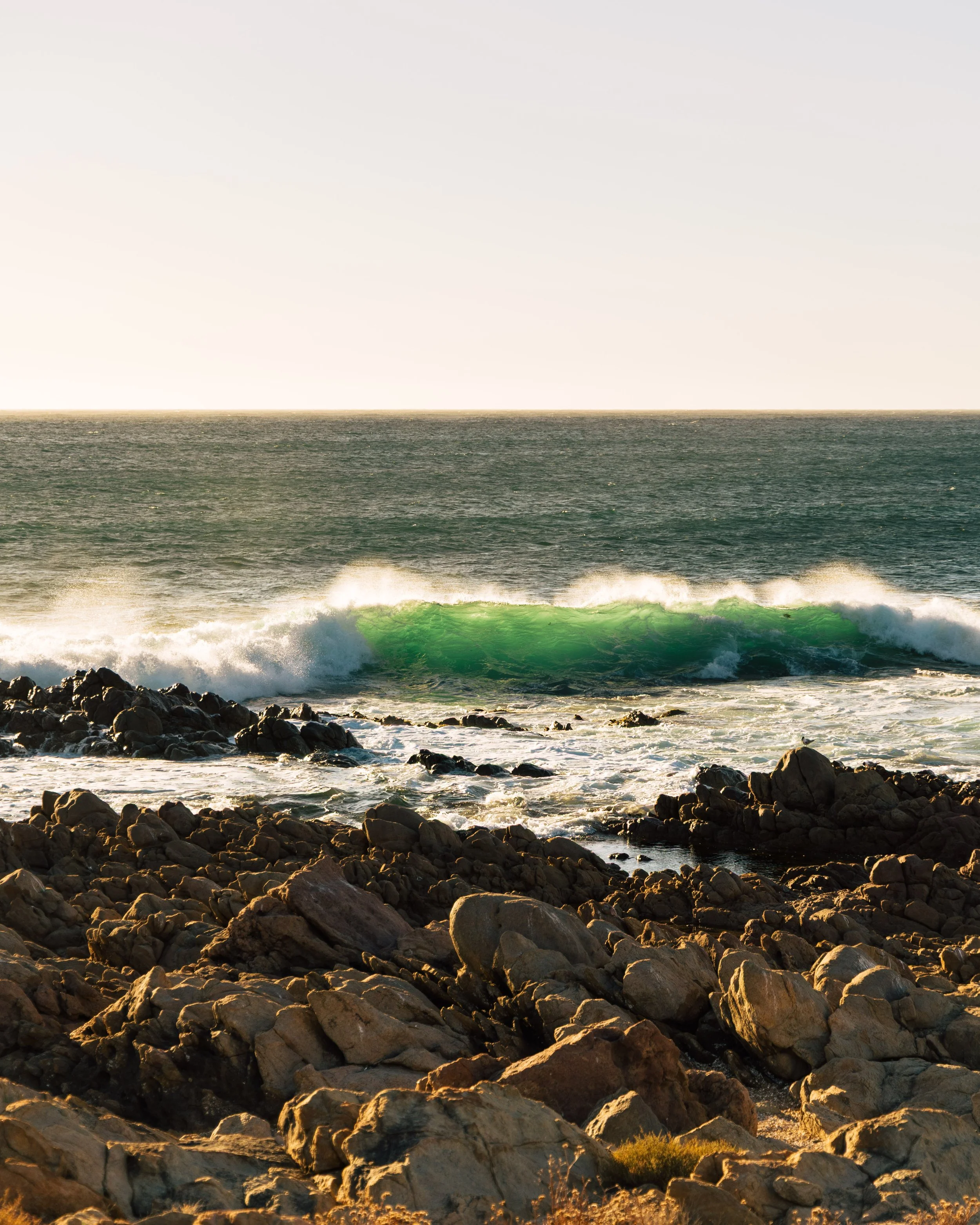 Rocks along the shoreline with ocean waves and horizon in the background during sunset or sunrise.