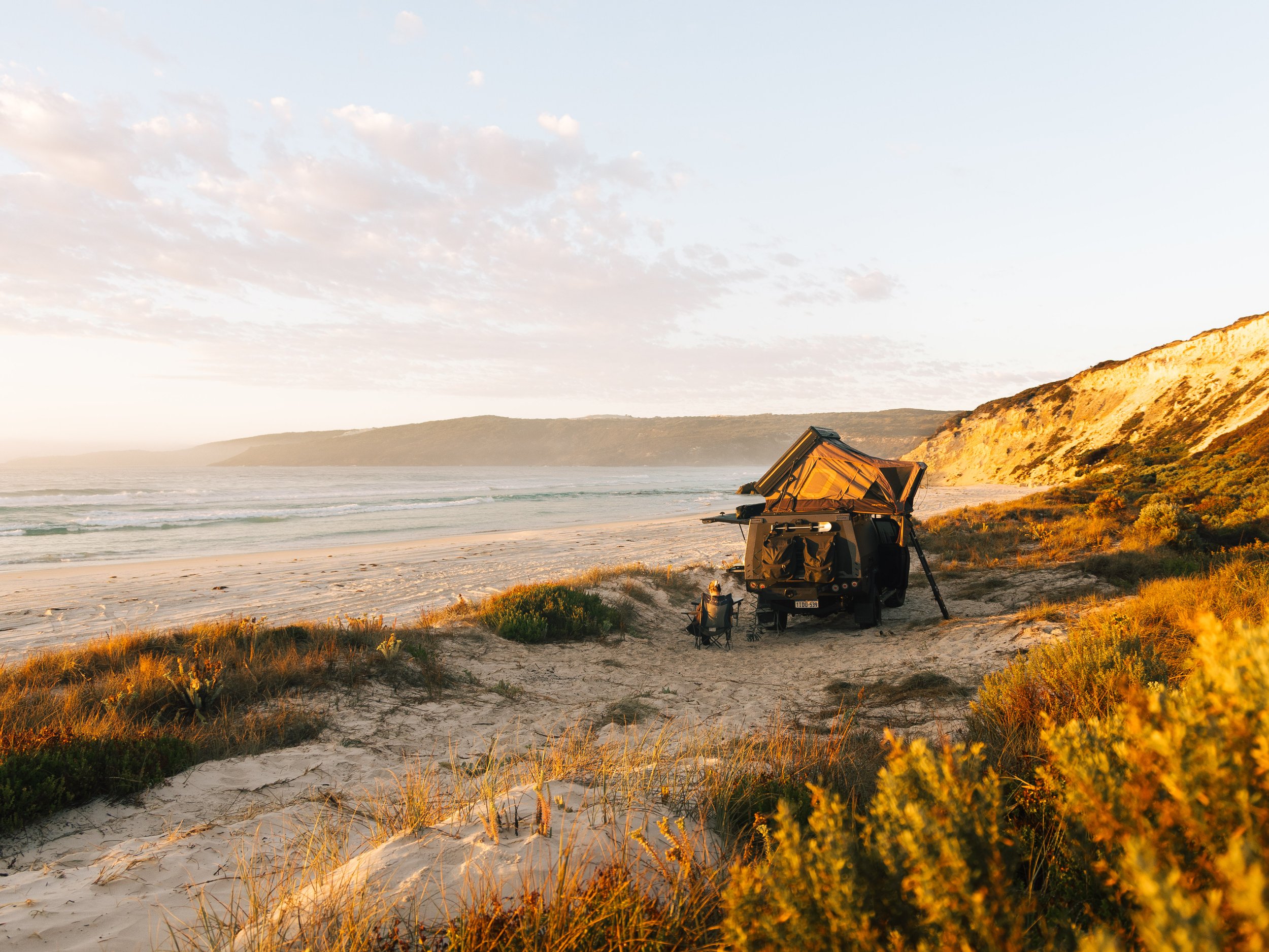 Sunset at a beach with dunes and grasses, with a suitcase and equipment set up for photography nearby.