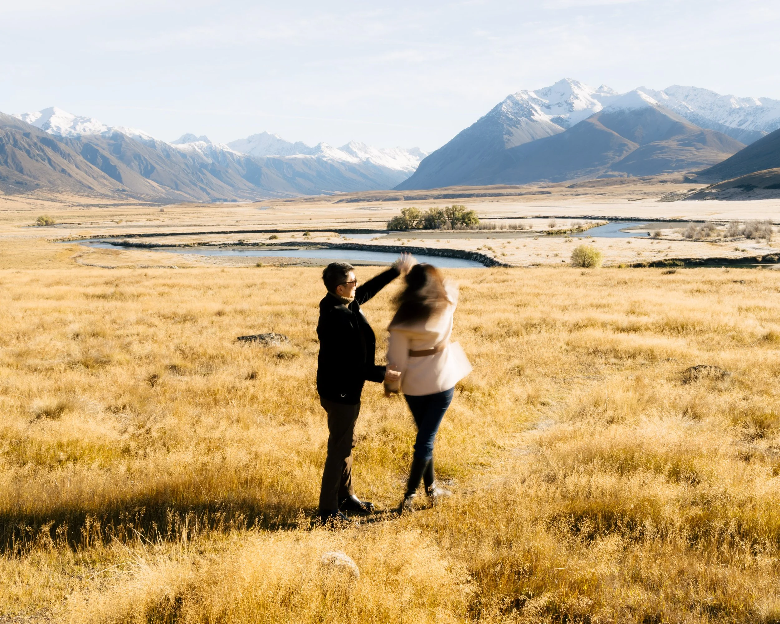 People in a field with mountains in the background, one person appears to be talking to a horse.