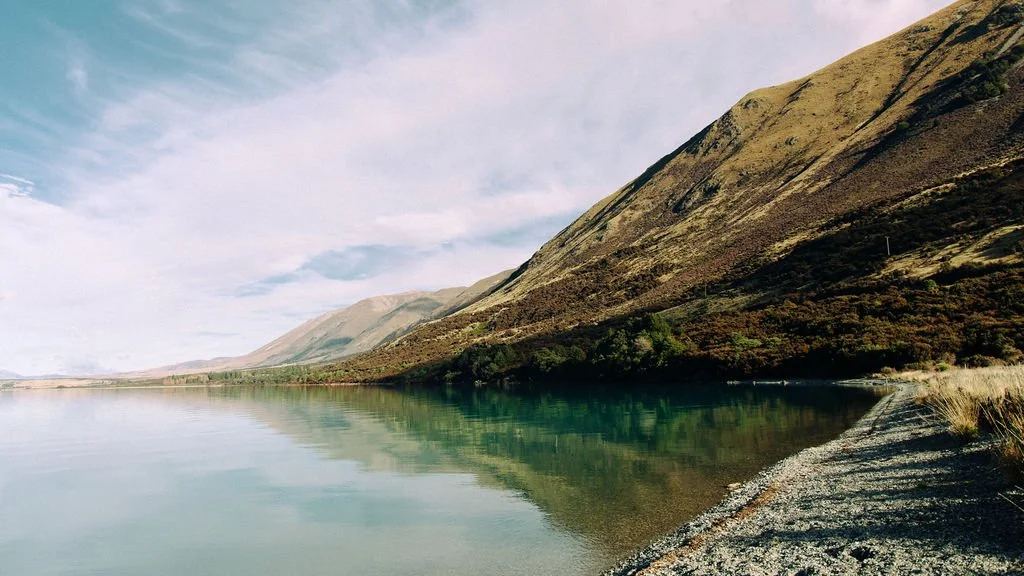 Scenic view of a calm lake with mountains in the background and a rocky shoreline to the right.