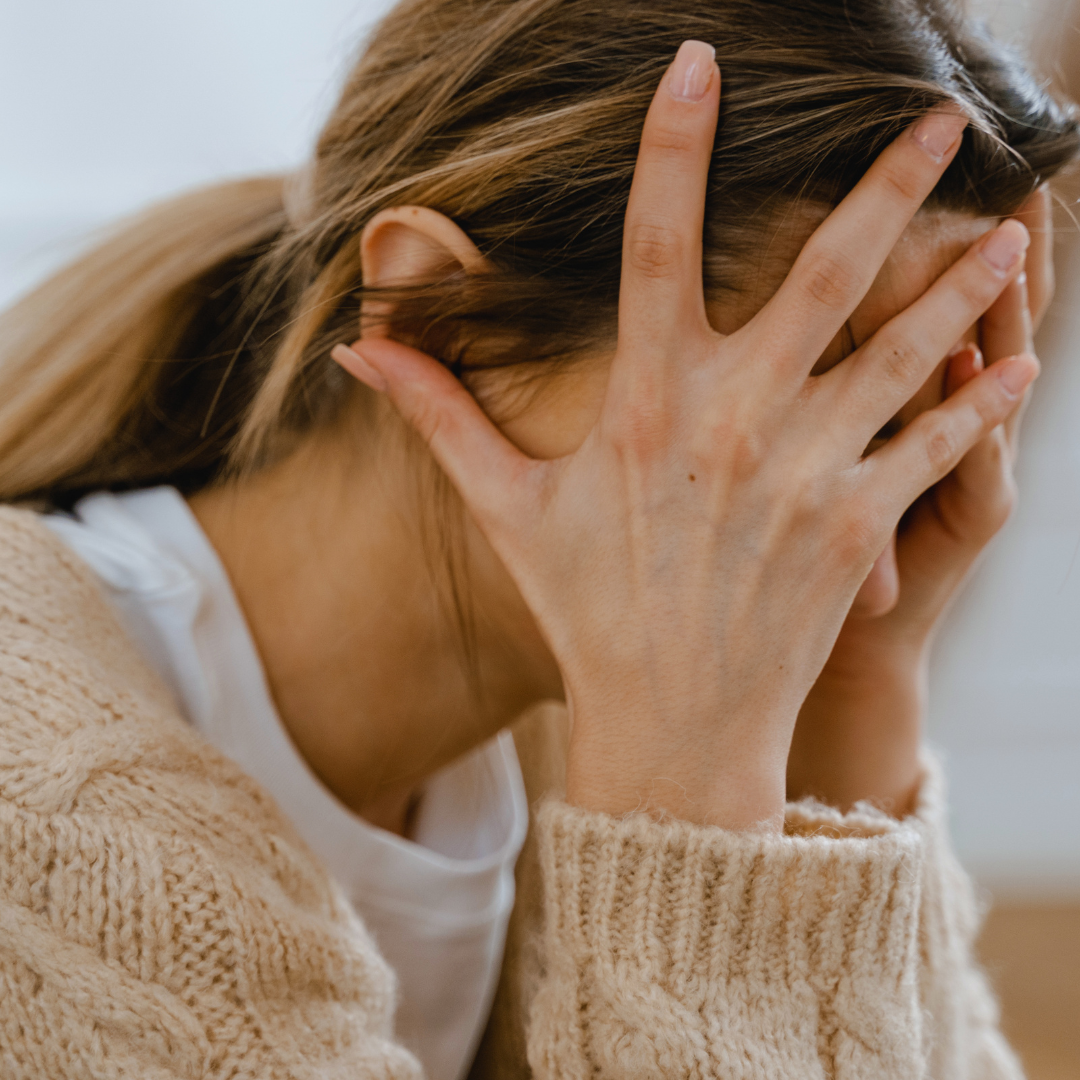 Woman with brown and blonde hair holding her face in her hand with distress.