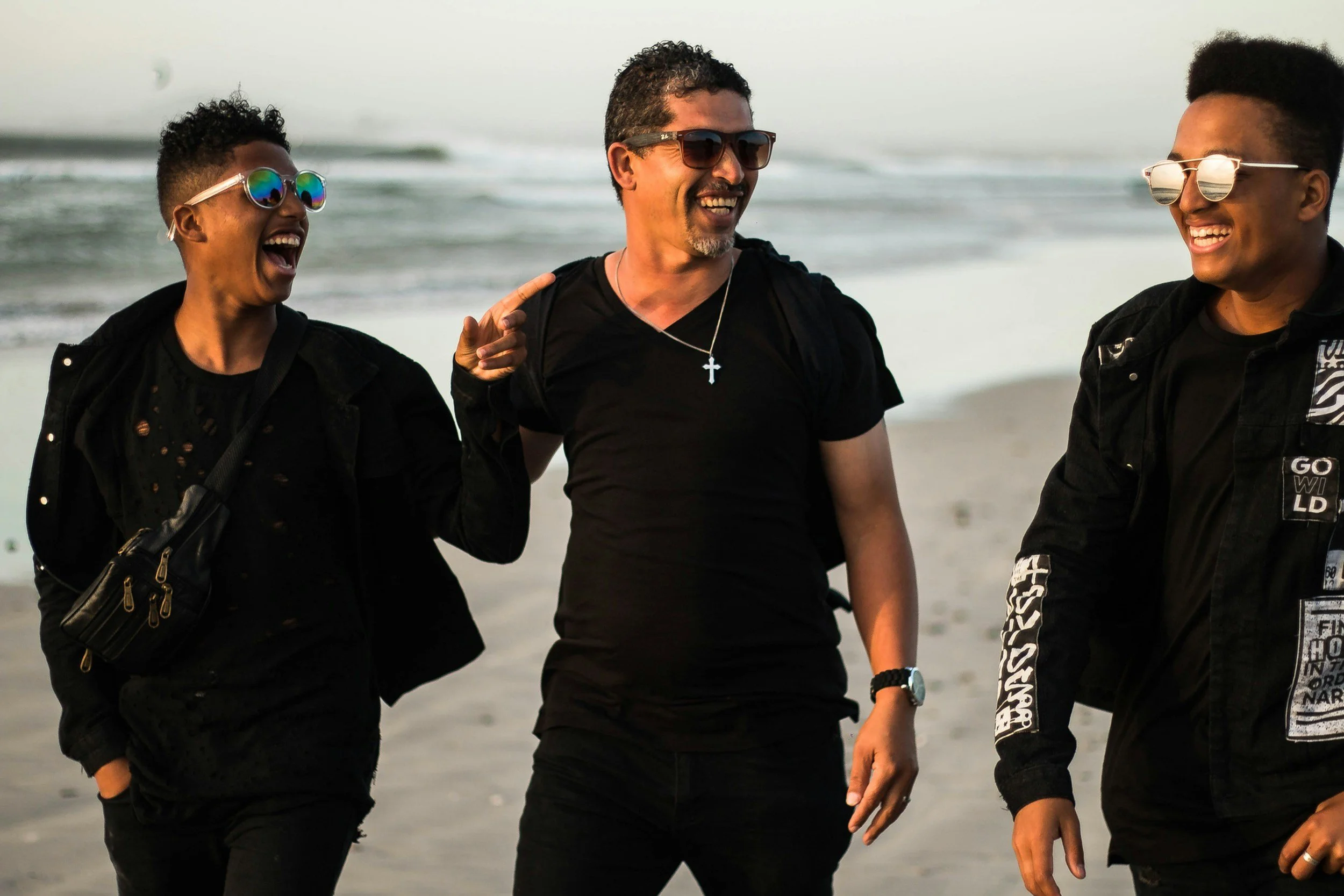 Three people smiling and laughing while walking on the beach.