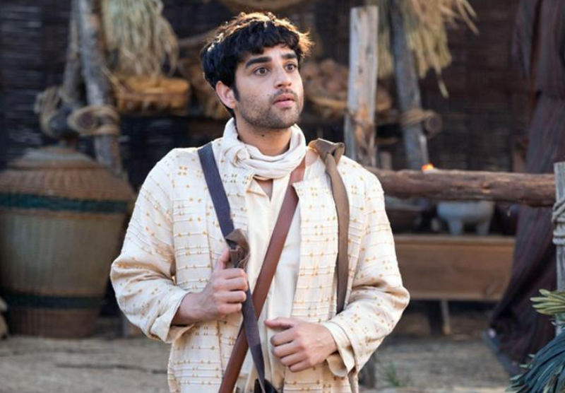 Matthew from The Chosen depicted with characteristics that suggest an autistic portrayal: he appears focused, with a thoughtful expression, a slightly detached demeanor, and is holding a pen and parchment, immersed in his work